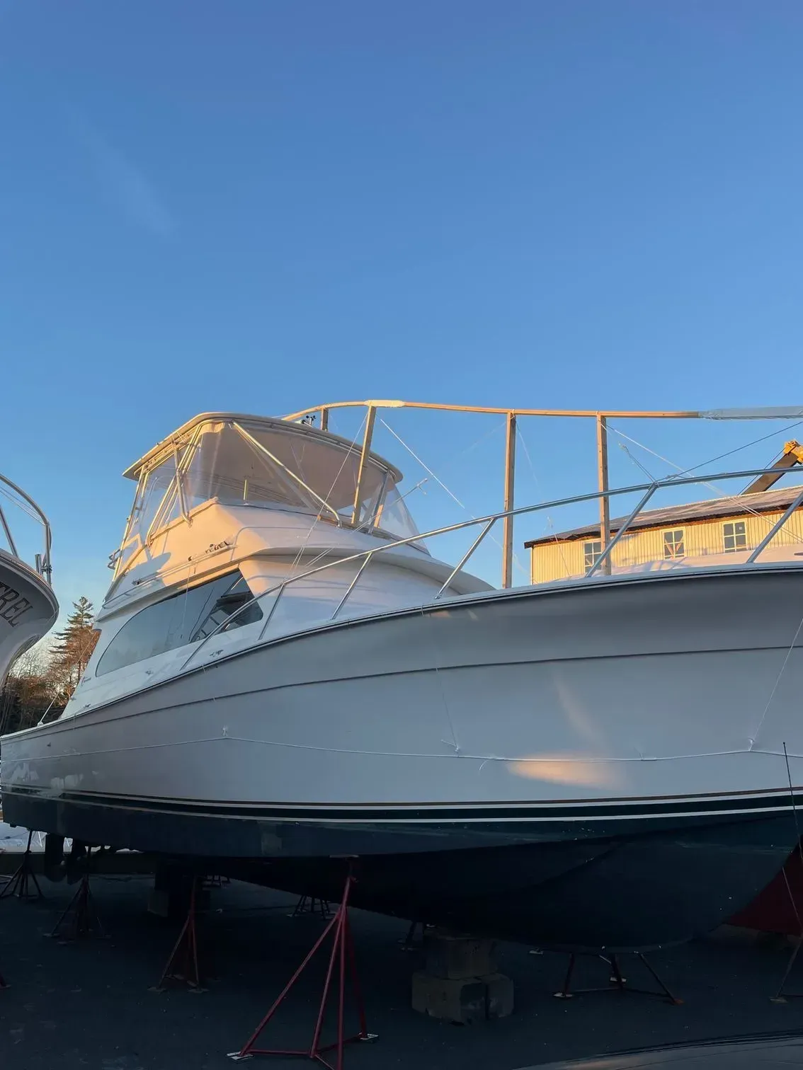 A white motor yacht resting on boat stands in a yard under a clear blue sky.