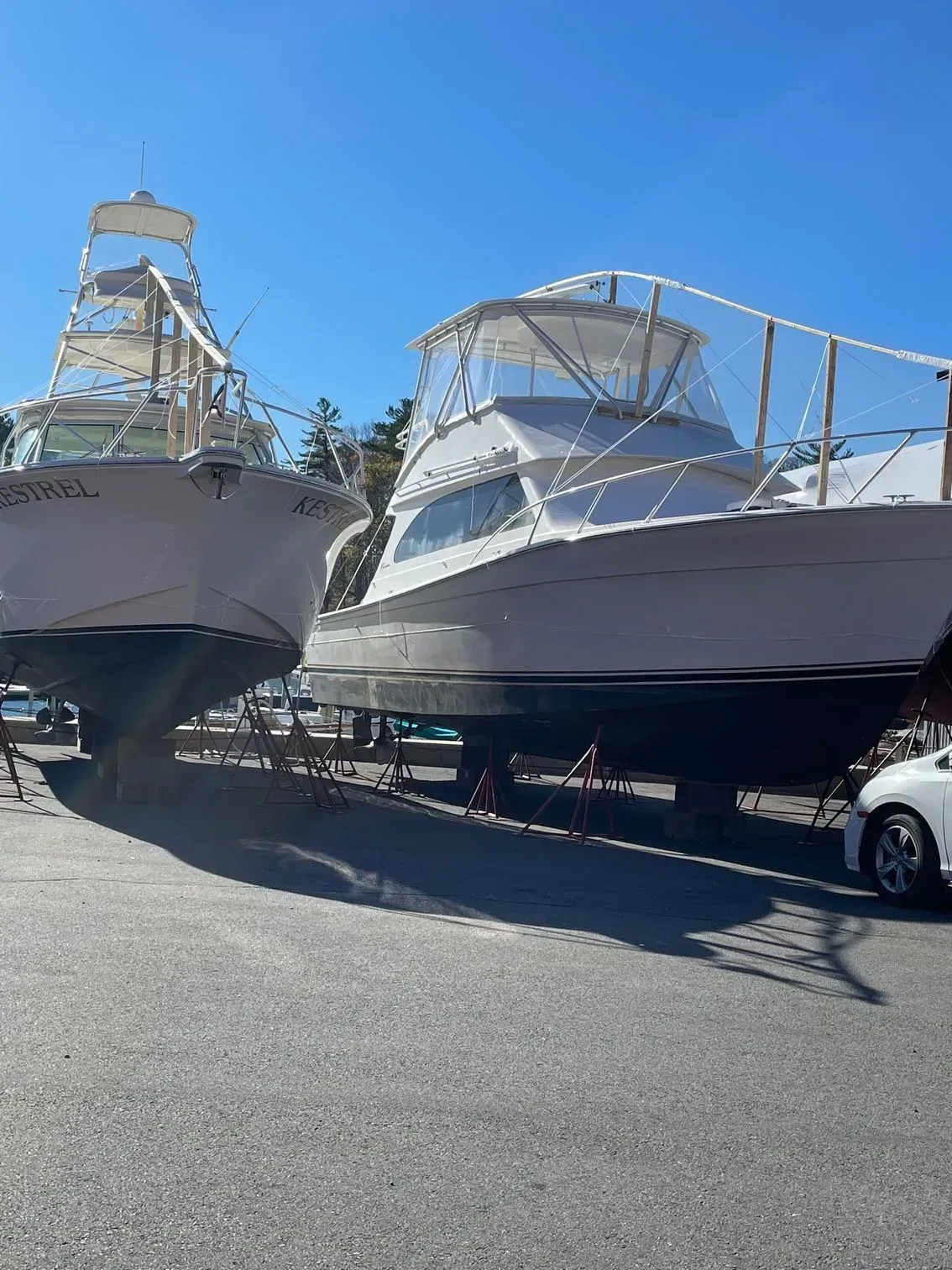 Two large white sport fishing boats propped up on supports in a sunny outdoor boat storage yard.