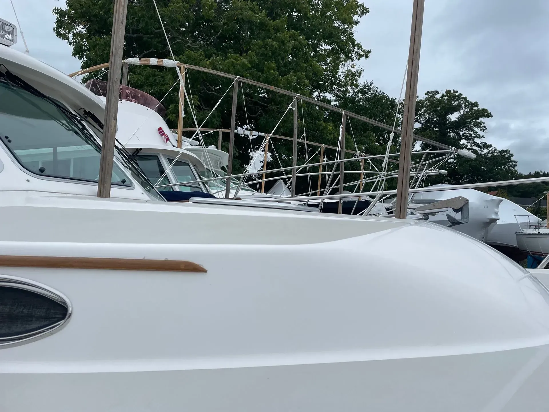 A close-up view of the white fiberglass bow and cabin window of a docked boat, with wooden support poles in the background.