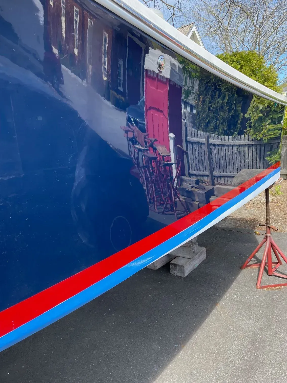 A glossy dark blue boat hull propped on jack stands, featuring red and blue pinstriping along the side.
