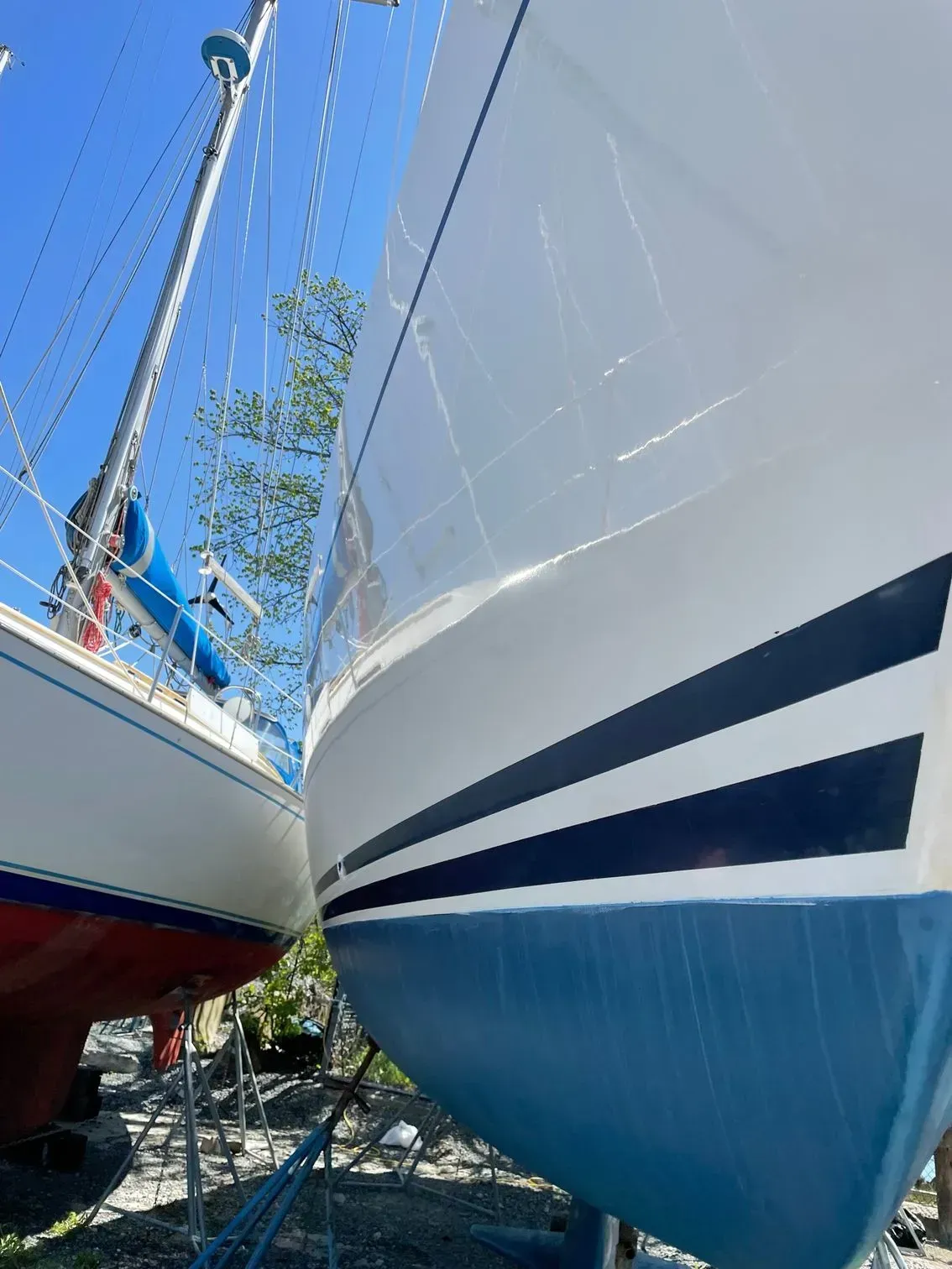 Two sailboats parked side-by-side in a boatyard on a sunny day.