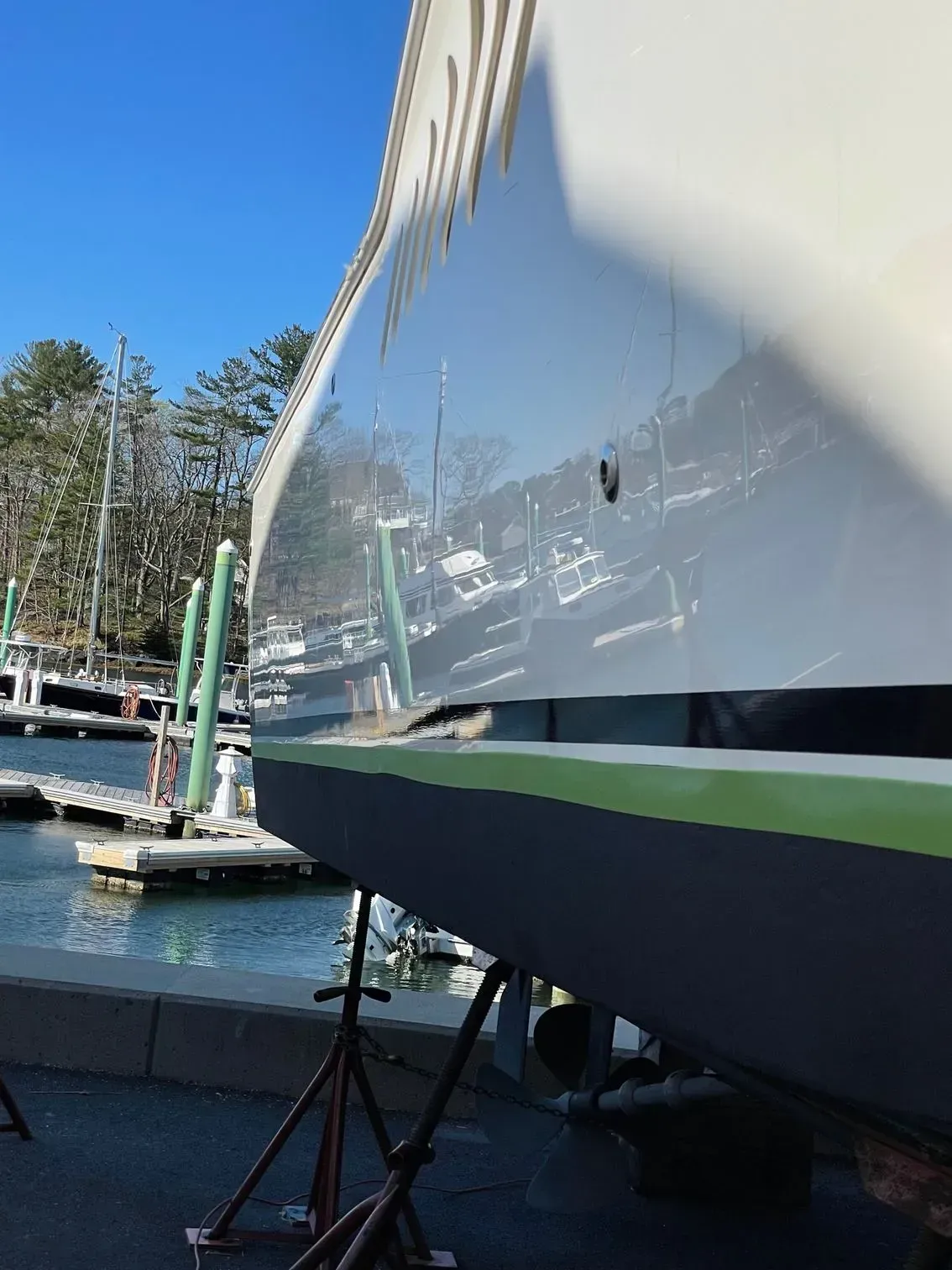 A boat hull on a stand at a marina, showing a white reflective surface above a black bottom with a green accent stripe.