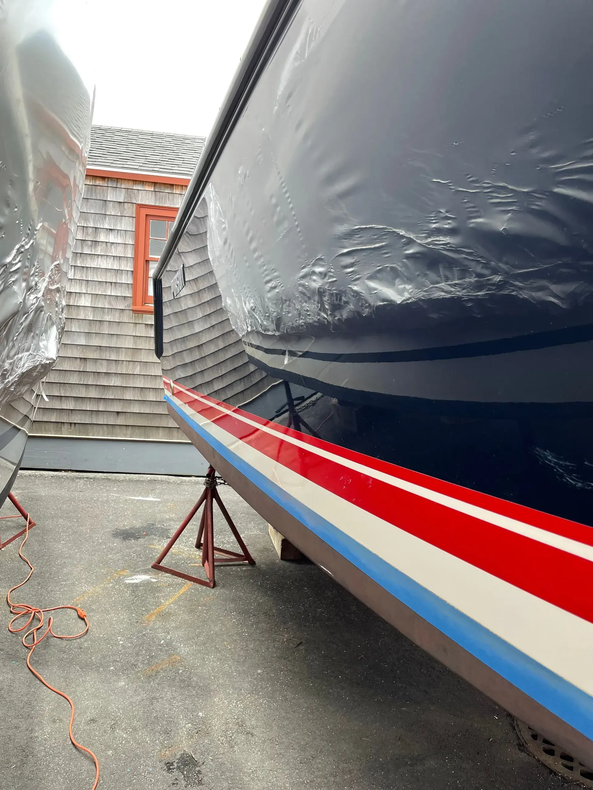 The hull of a boat in dry dock, showing its navy blue, red, and blue painted stripes, resting on metal support jacks.