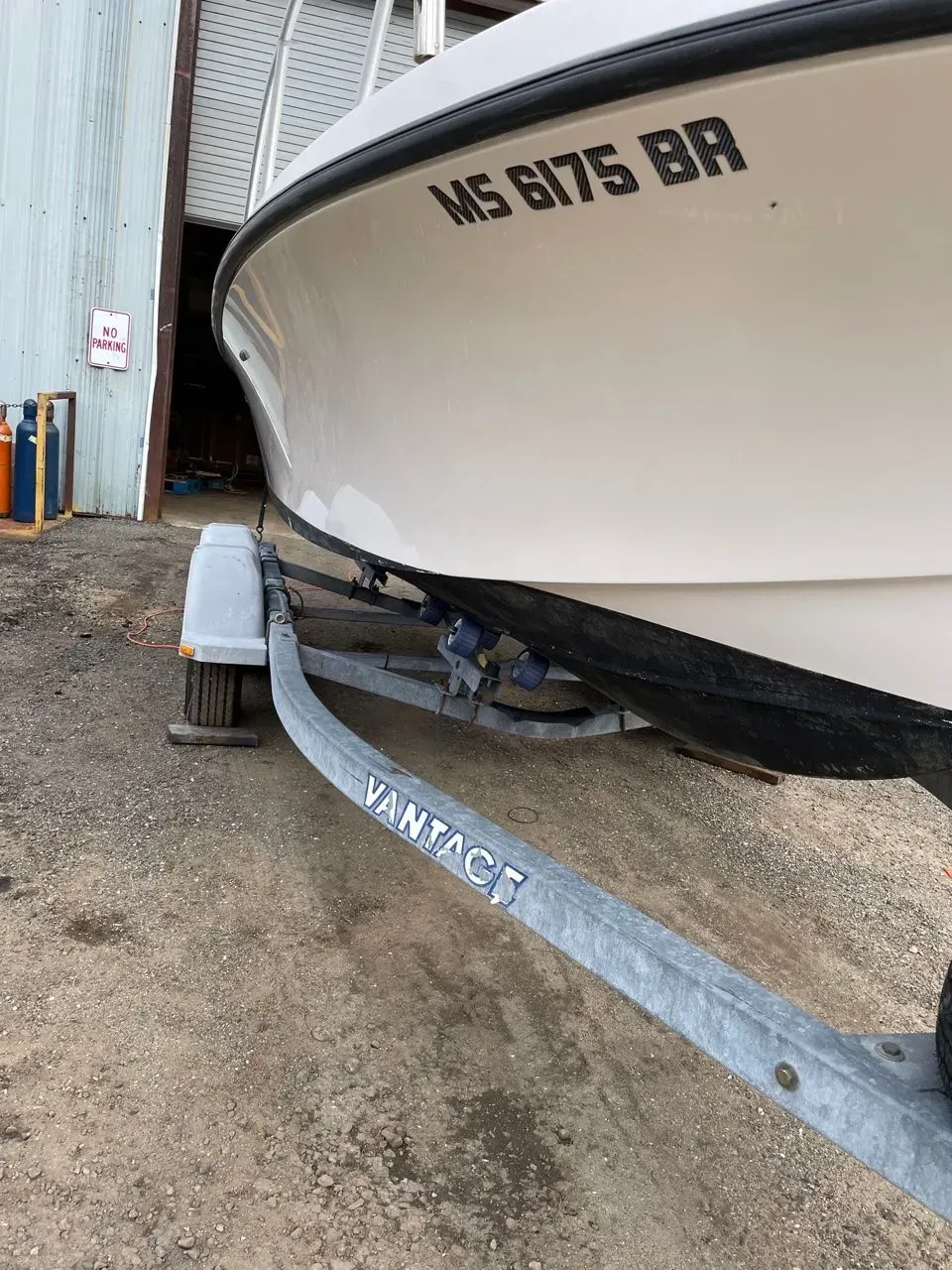 A white boat on a metal trailer parked on a gravel surface, with the registration number MS 6175 BR visible on the hull.