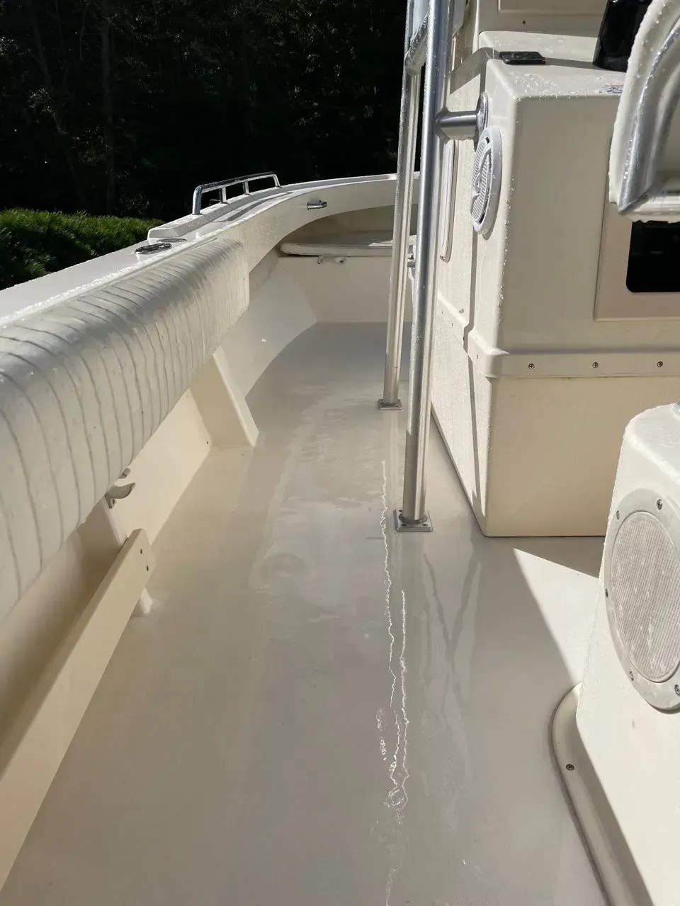 A side view of a beige boat deck, showing a clean, narrow walkway, seating, and a speaker on the side of the center console.