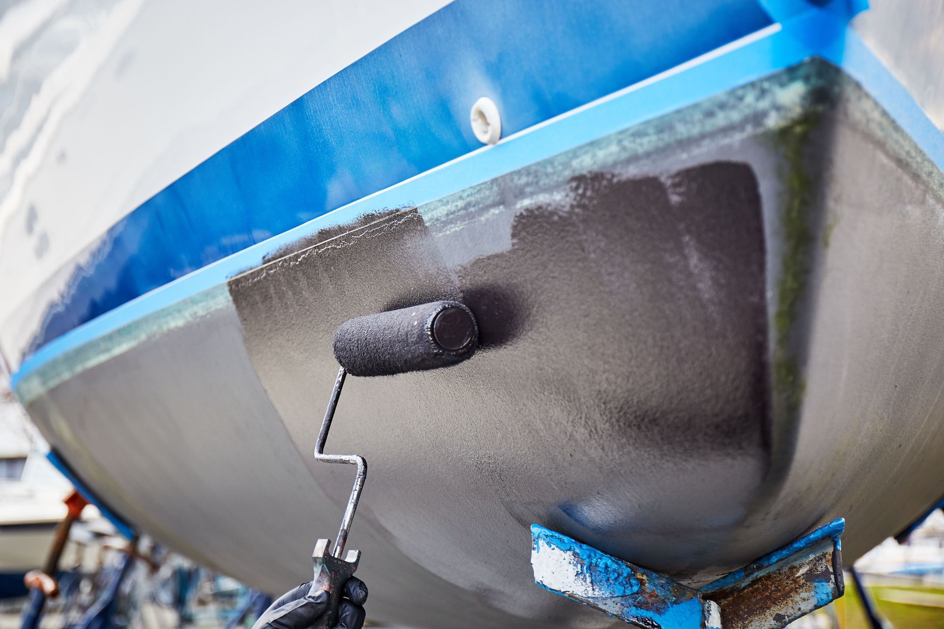 Boat hull being painted black with a roller.