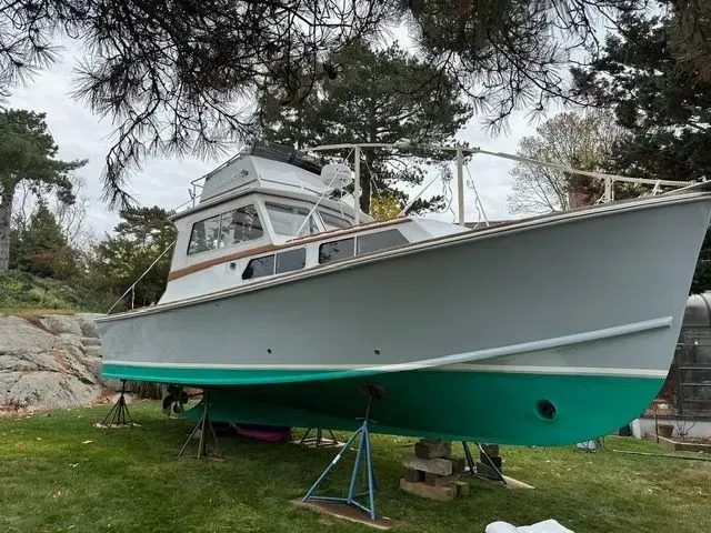 Gray boat with teal bottom on land, supported by stands, near trees and greenery.