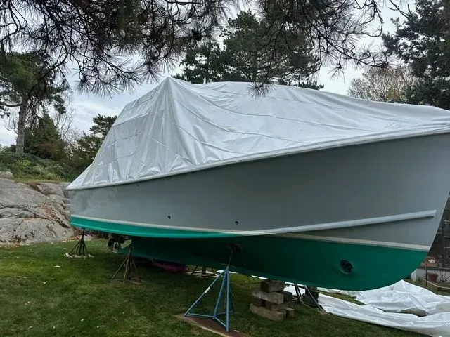 Gray boat covered with a white tarp on grass. Green hull.