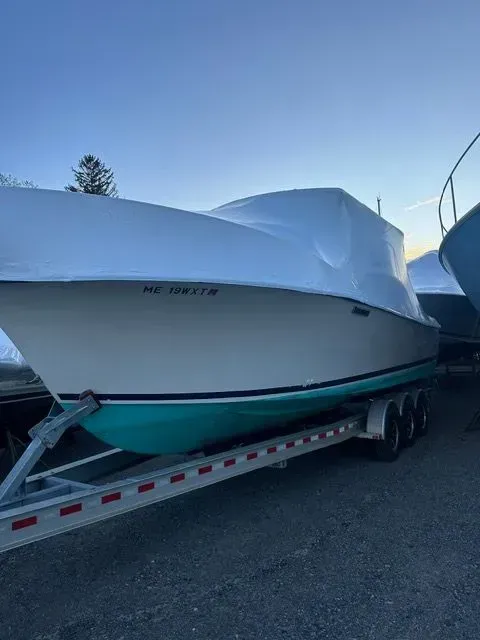 Boat on a trailer, covered with a white tarp, teal hull, parked outside, against a blue sky.