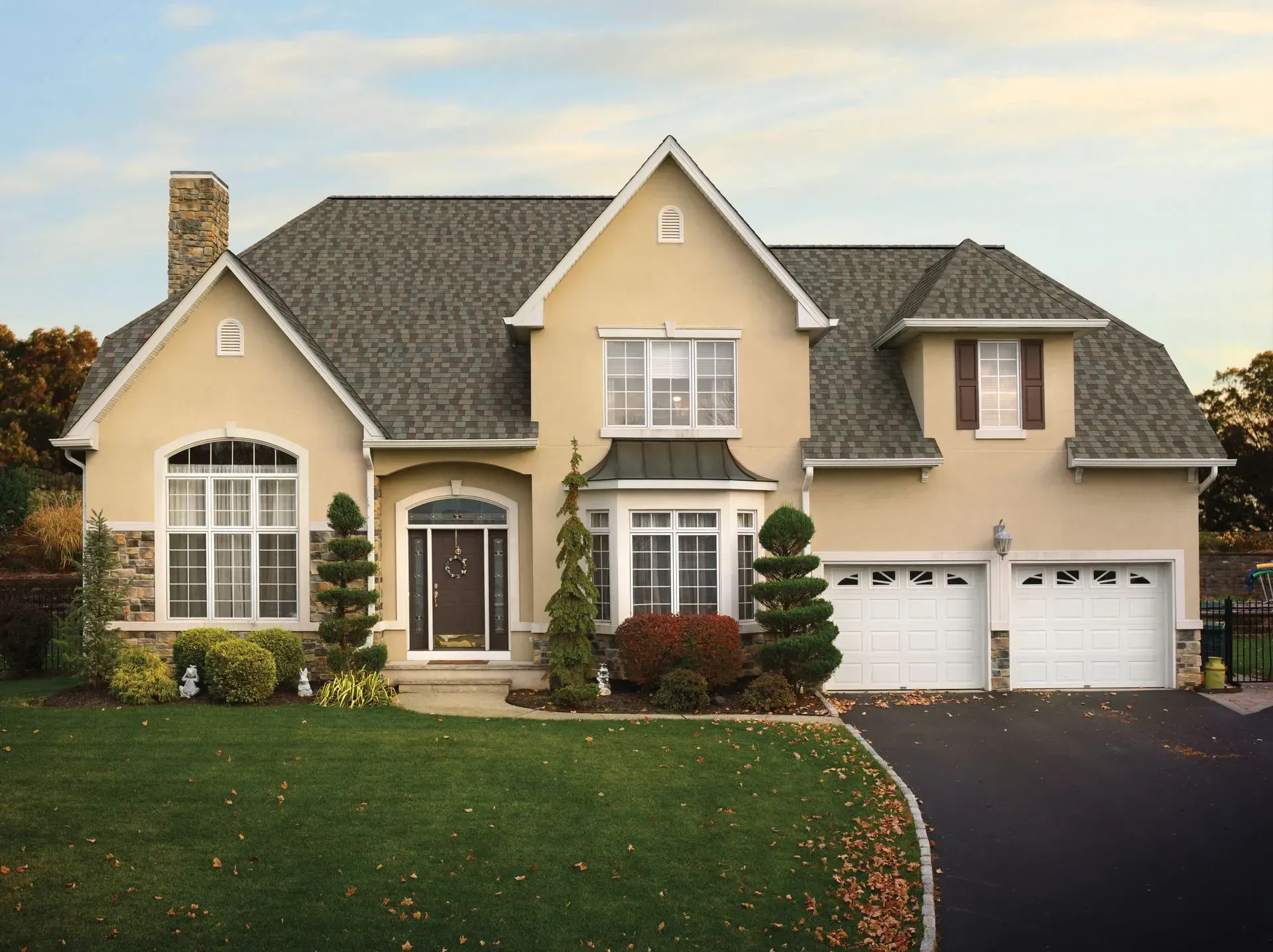 Beige two-story house with a green lawn, black driveway, and a garage.