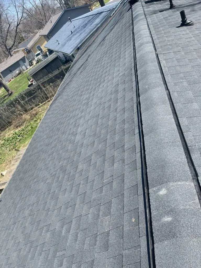 Gray asphalt shingle roof with a black ridge cap, seen from above, outdoors.