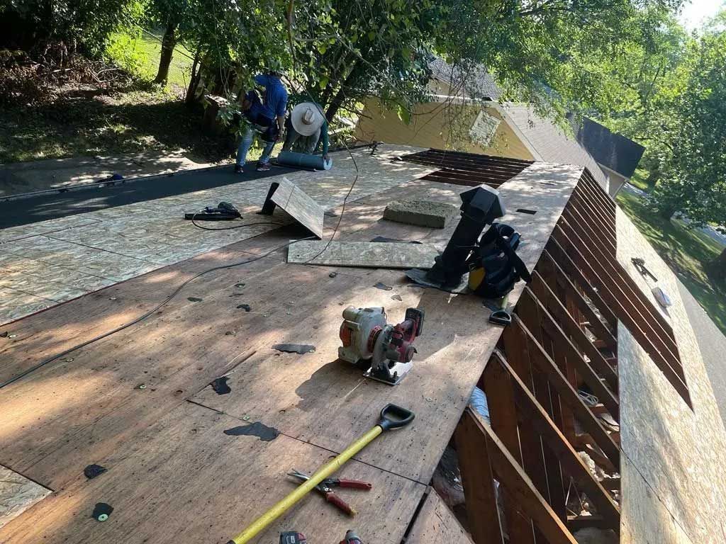 Roof being repaired: Workers, tools, and new plywood on the roof. Sunny day.