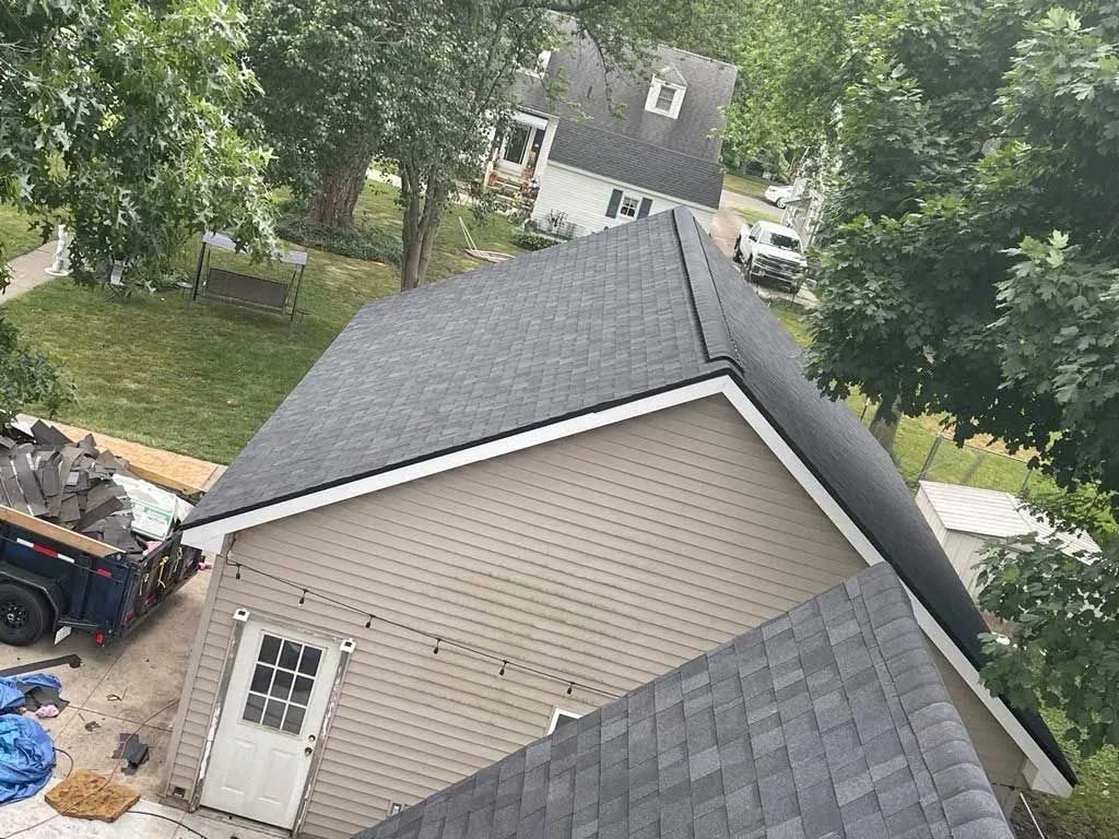 A building with a newly installed grey shingle roof and tan siding, viewed from above.