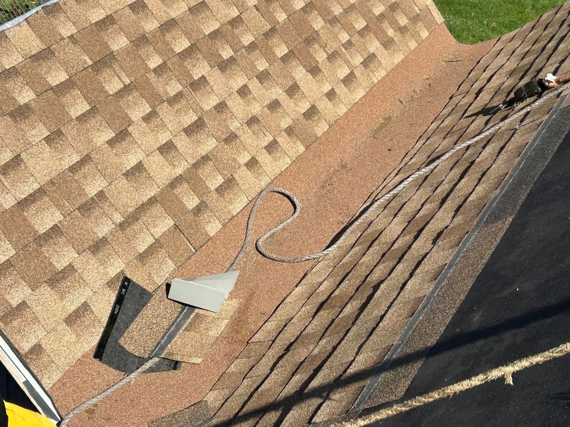 A roof with brown shingles and a dark, debris-filled valley, a wire runs across it.