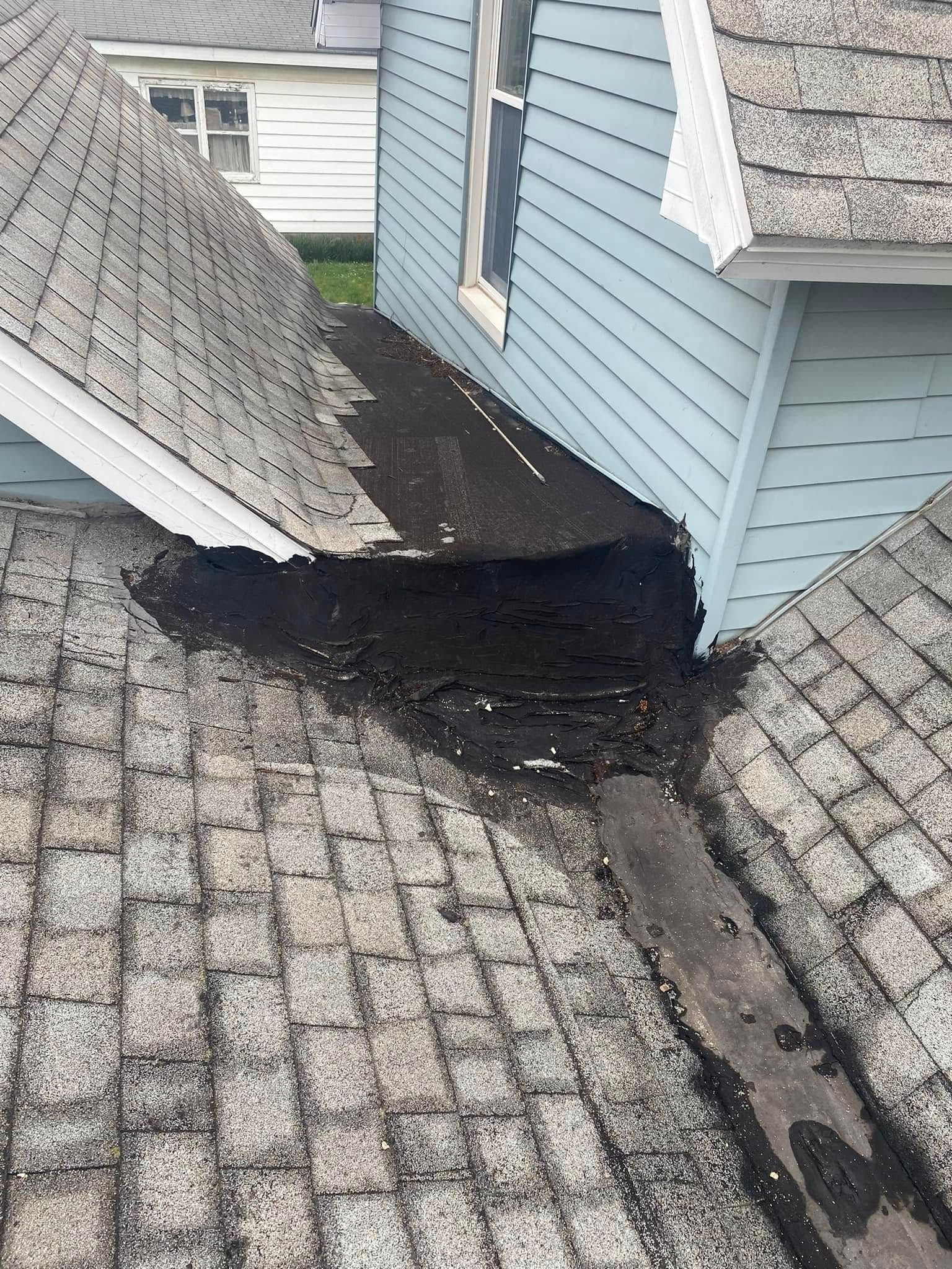 Damaged asphalt shingles and roof flashing at the junction of two roof sections, likely causing leaks.