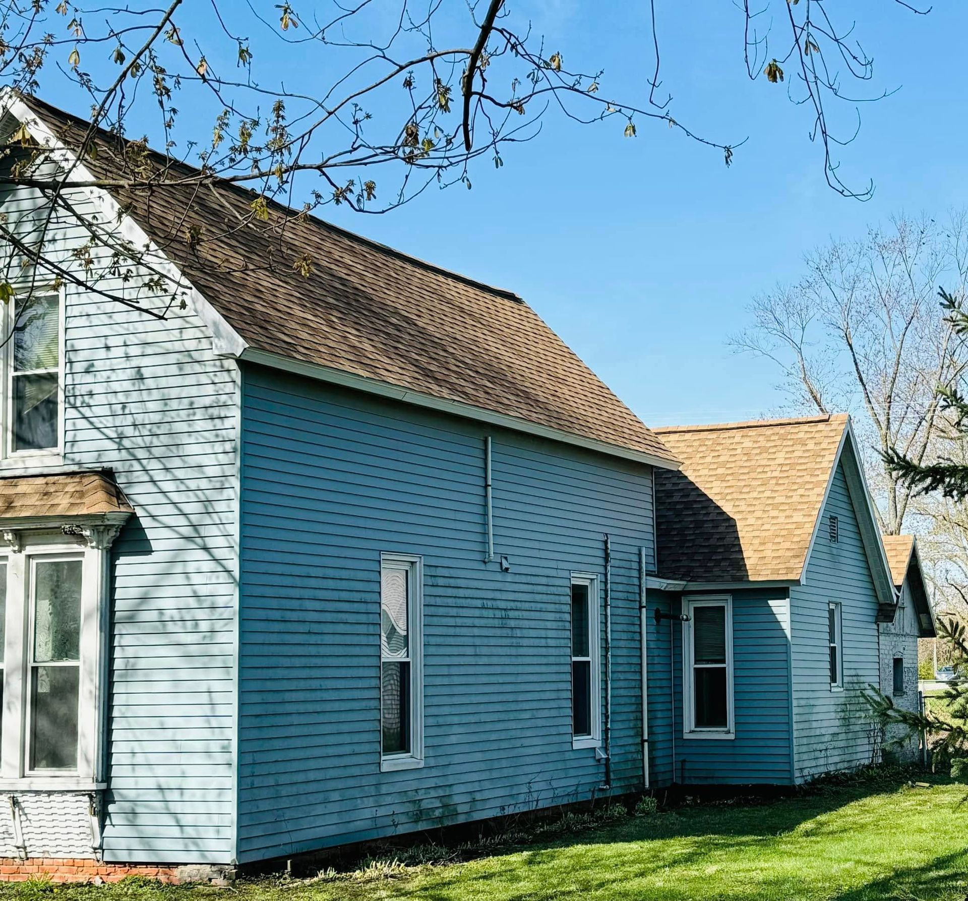 Blue house with brown roof on a sunny day, seen from a grassy yard.