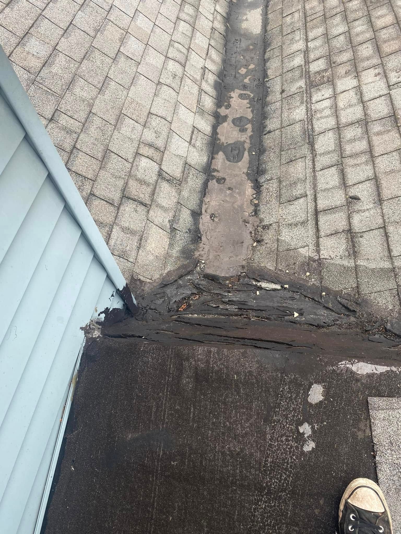 Overhead view of a roof with shingles and a dark sealant covering a seam near blue siding.