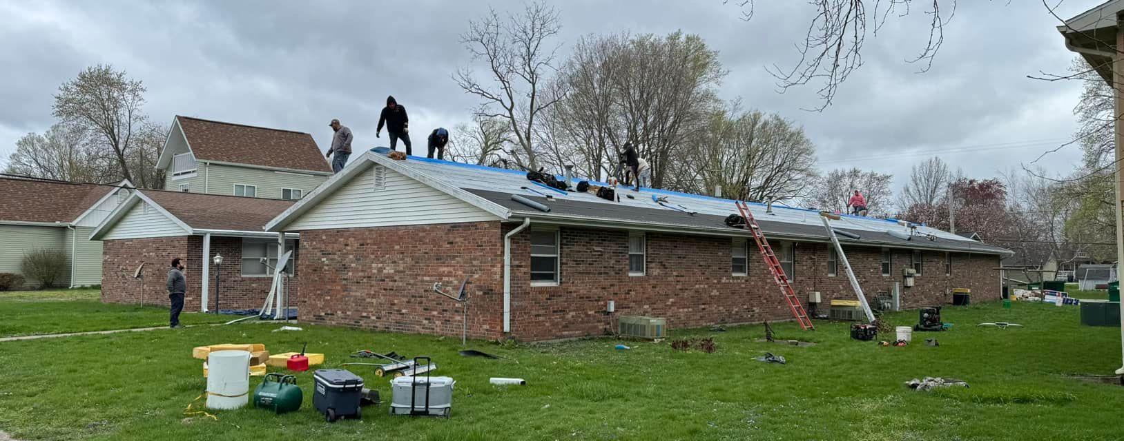 Construction workers on a brick building's roof with tools and ladders. Overcast day.