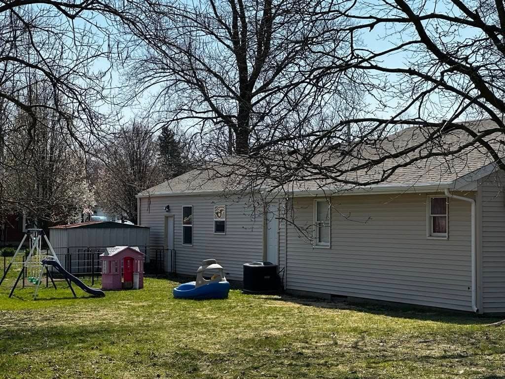 Backyard with swing set, playhouse, and small pool by a white house on a sunny day.
