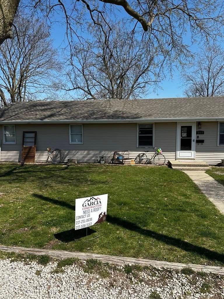 Low beige house, lawn, sign, bicycles in front. Blue sky, trees.