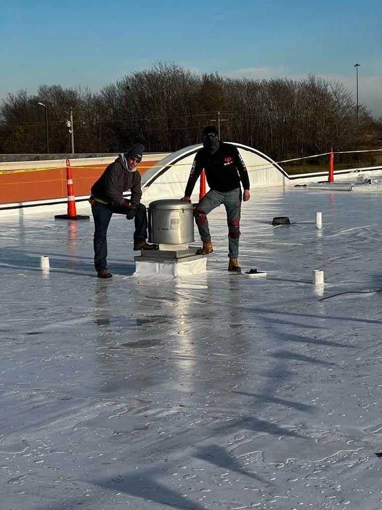 Two workers on a reflective white roof. One stands by a vent. Both are wearing jeans and work boots.