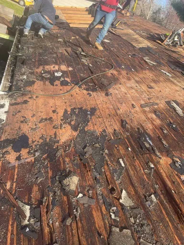 Roofing crew tearing off an old, damaged roof with exposed wooden boards.