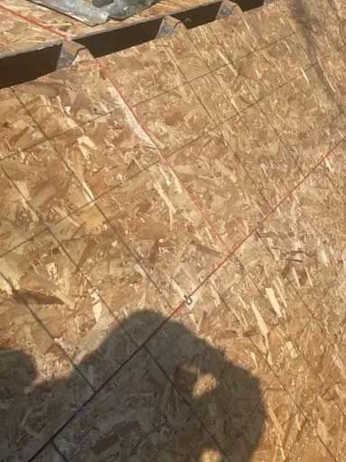 OSB roof decking with lines, shadowed person, partially completed roof construction.