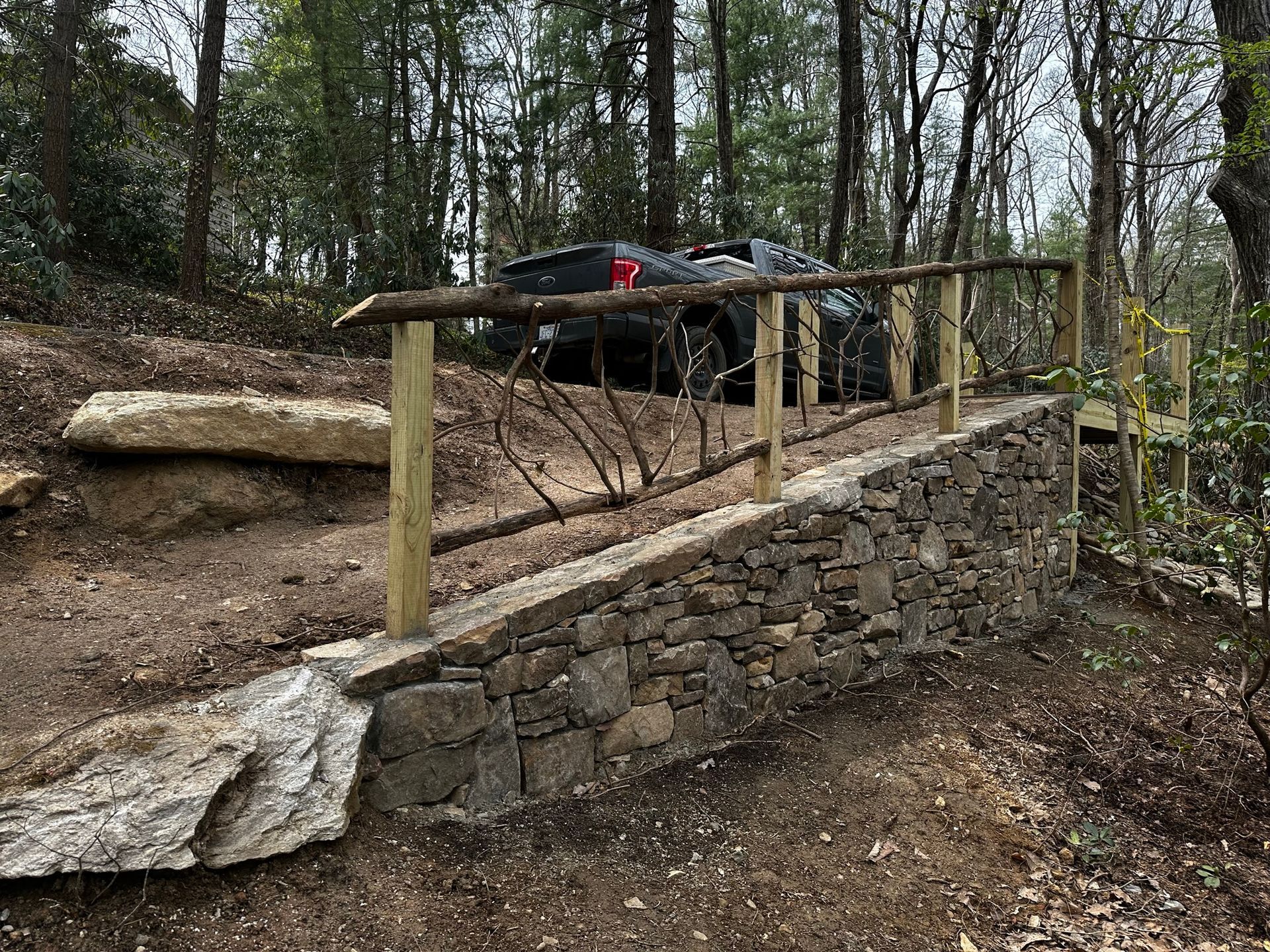 A truck is parked in the woods next to a stone wall.