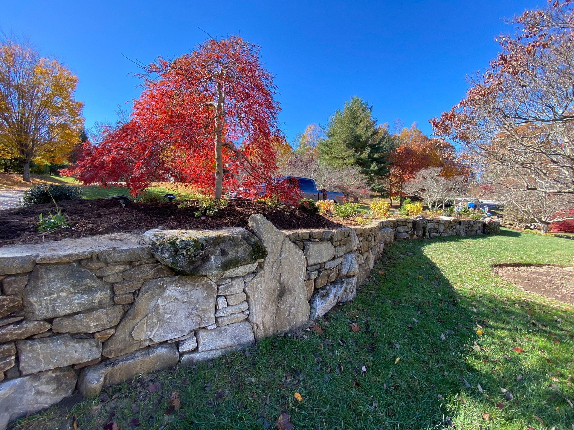 A stone wall surrounds a lush green field with trees in the background.