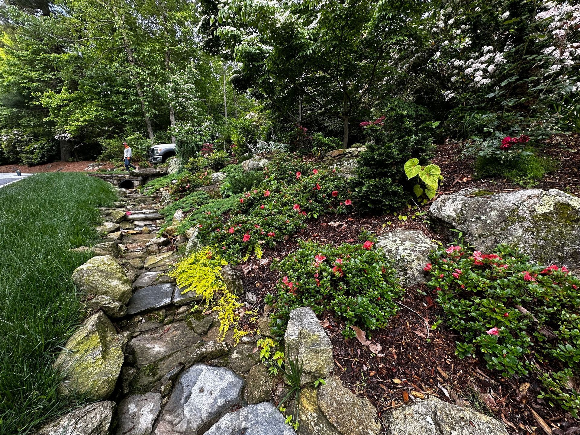 A stone path in a garden surrounded by trees and flowers.