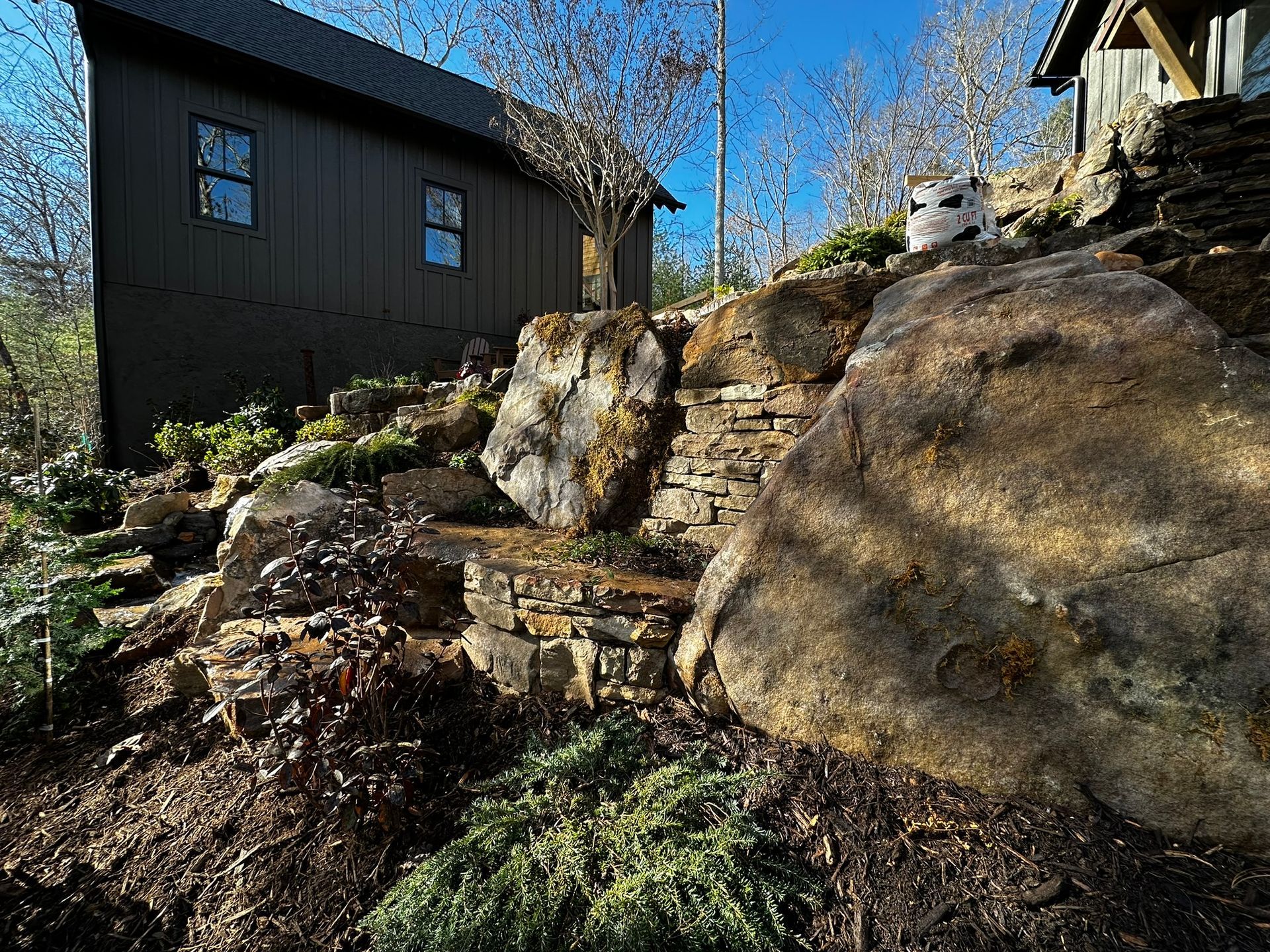 A house is sitting on top of a rocky hill next to a large rock.