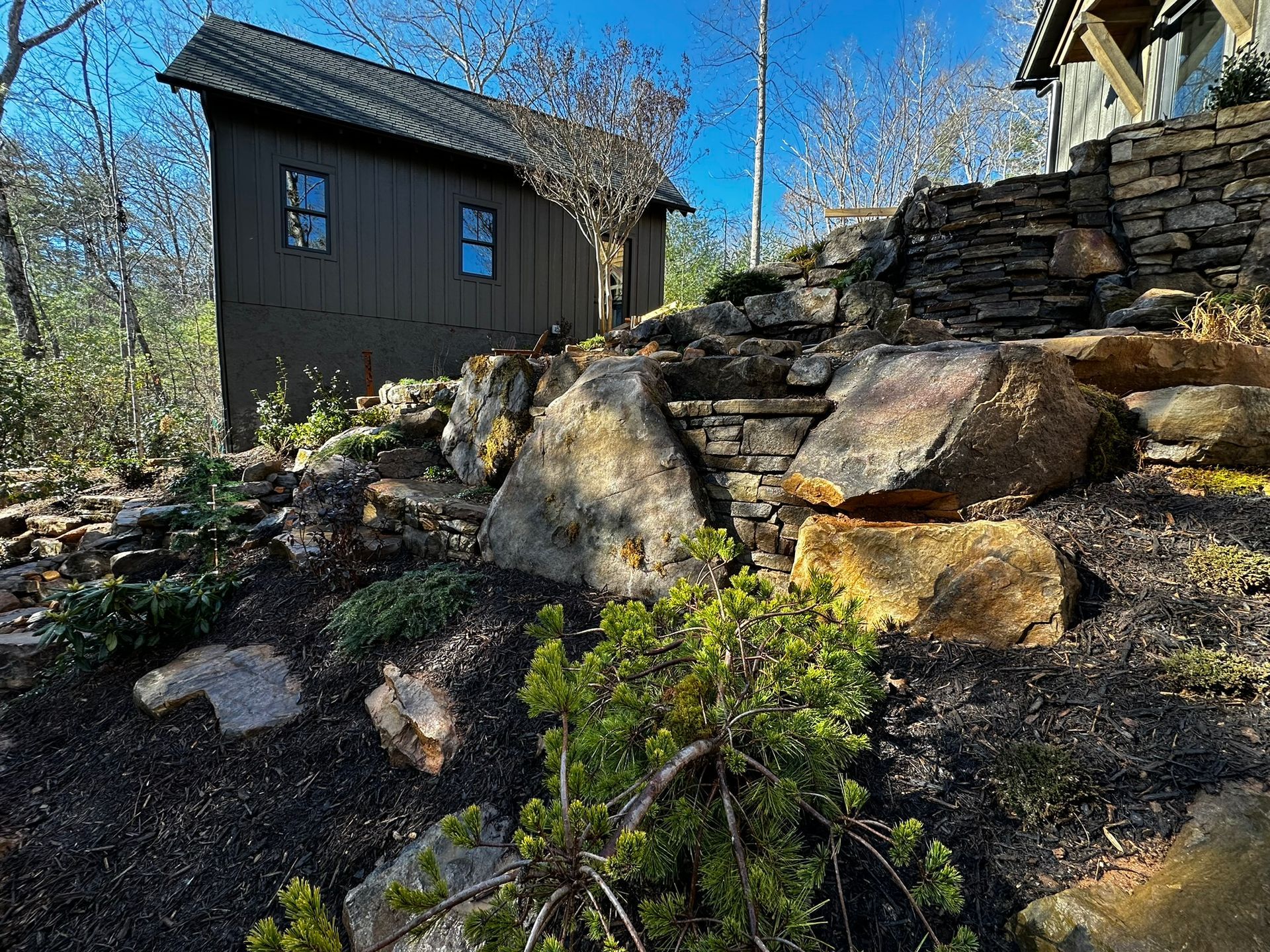 A house is sitting on top of a rocky hill next to a stone wall.