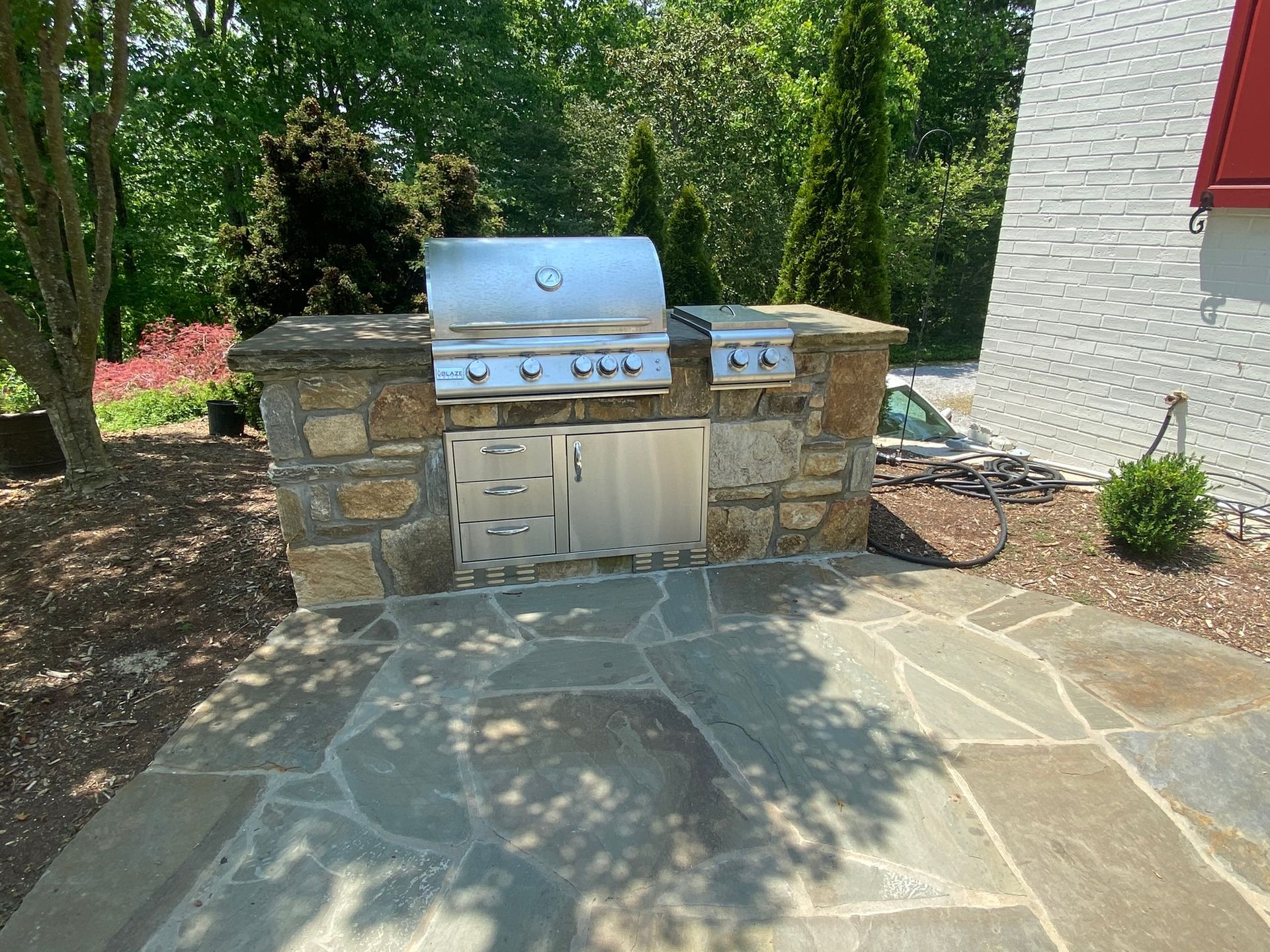 A grill is built into a stone wall in the backyard of a house.