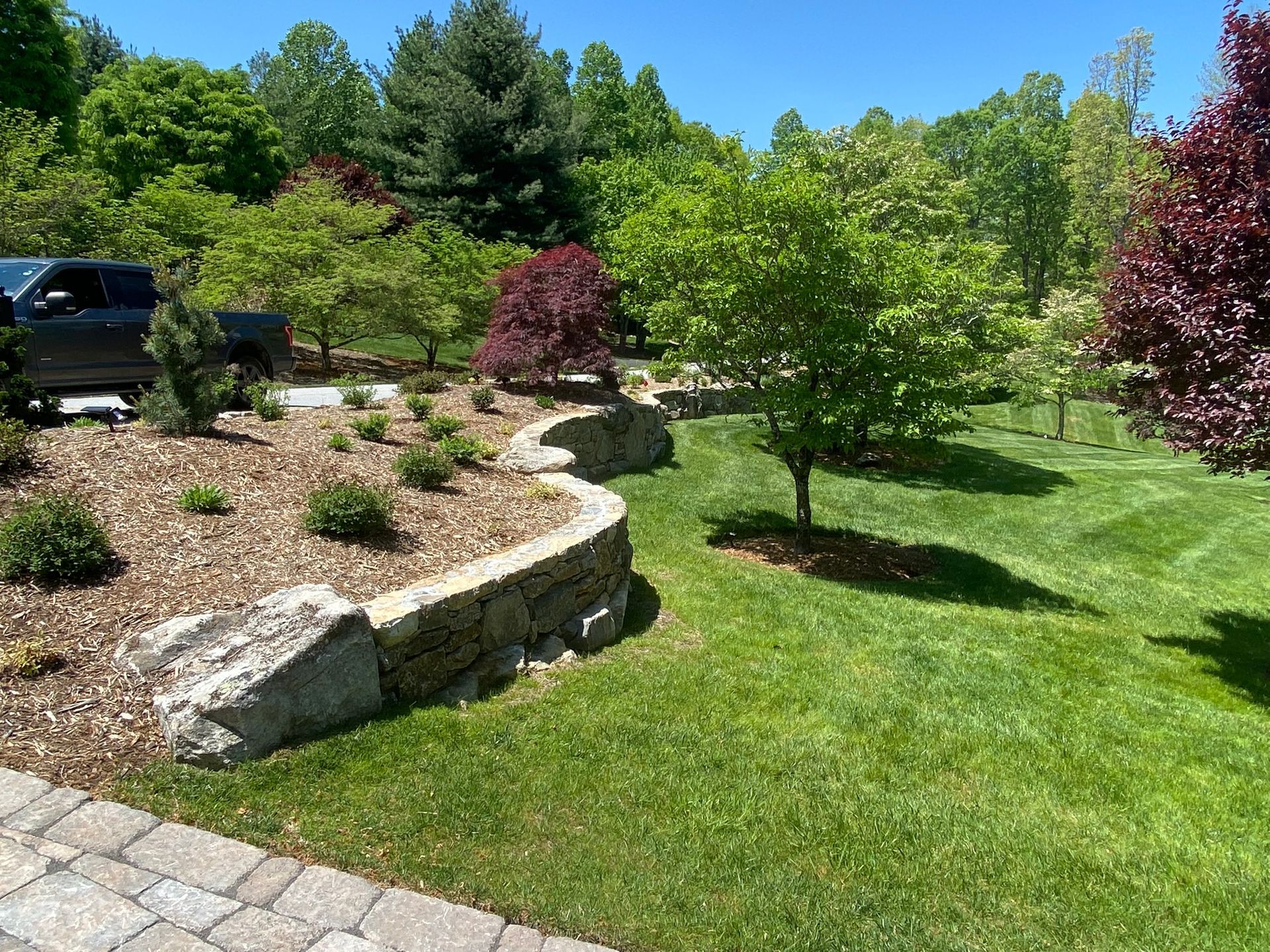 A lush green lawn with a stone wall and a car parked in the background.