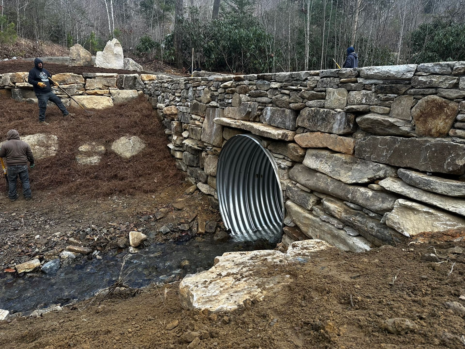 A man is working on a stone wall next to a metal pipe.