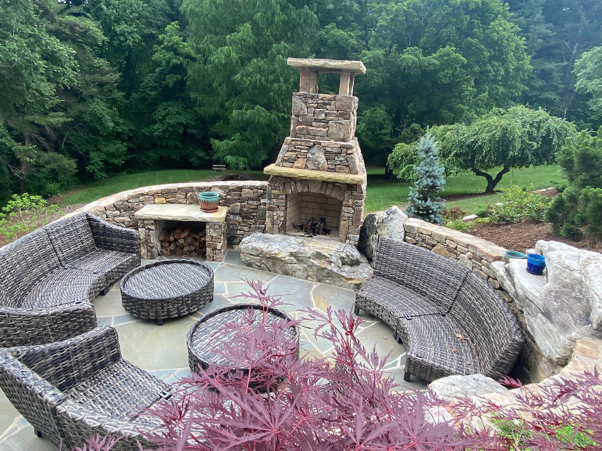 There is a fireplace in the middle of the patio surrounded by wicker furniture.