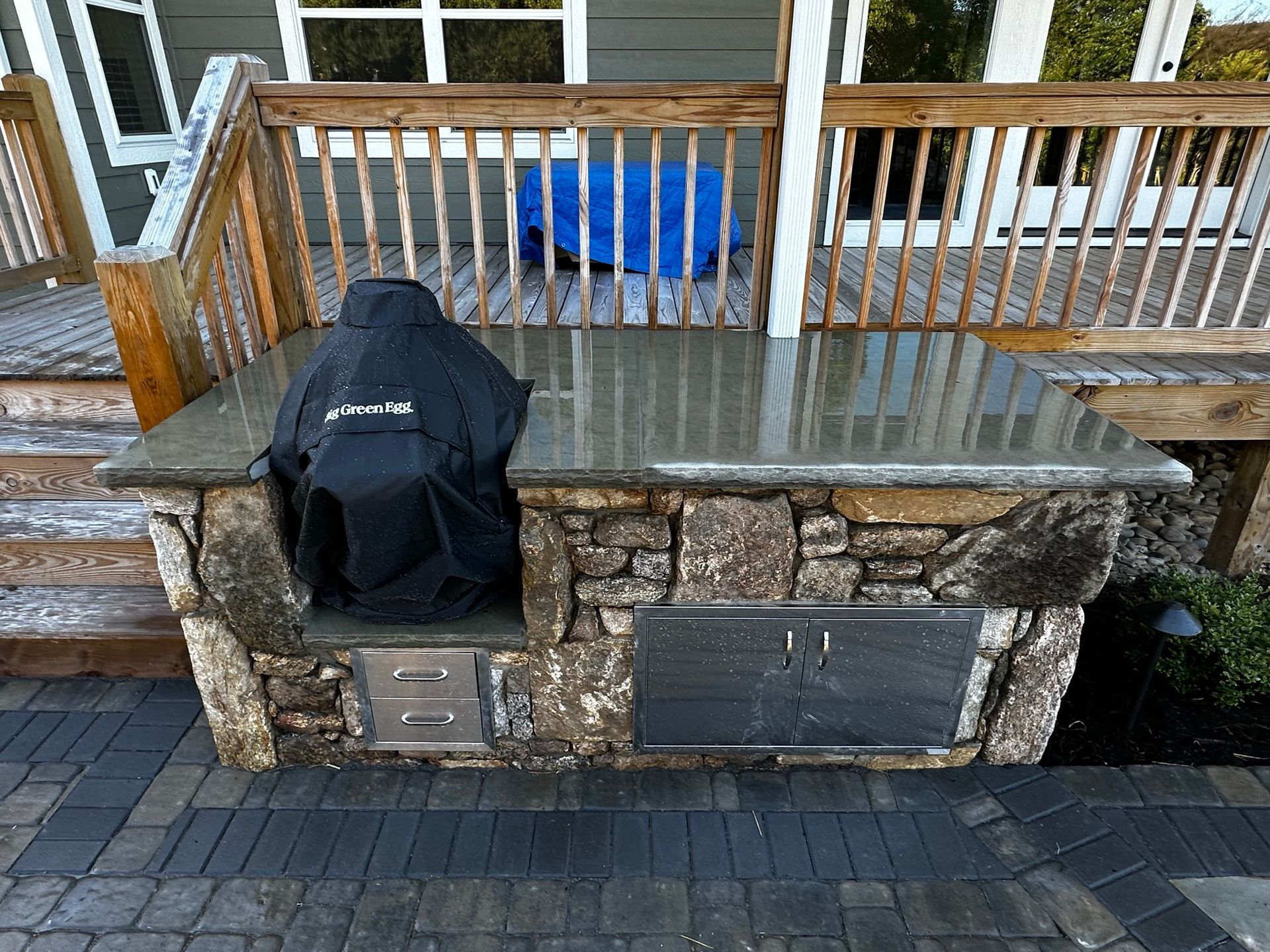 A grill is sitting on top of a stone counter next to a deck.