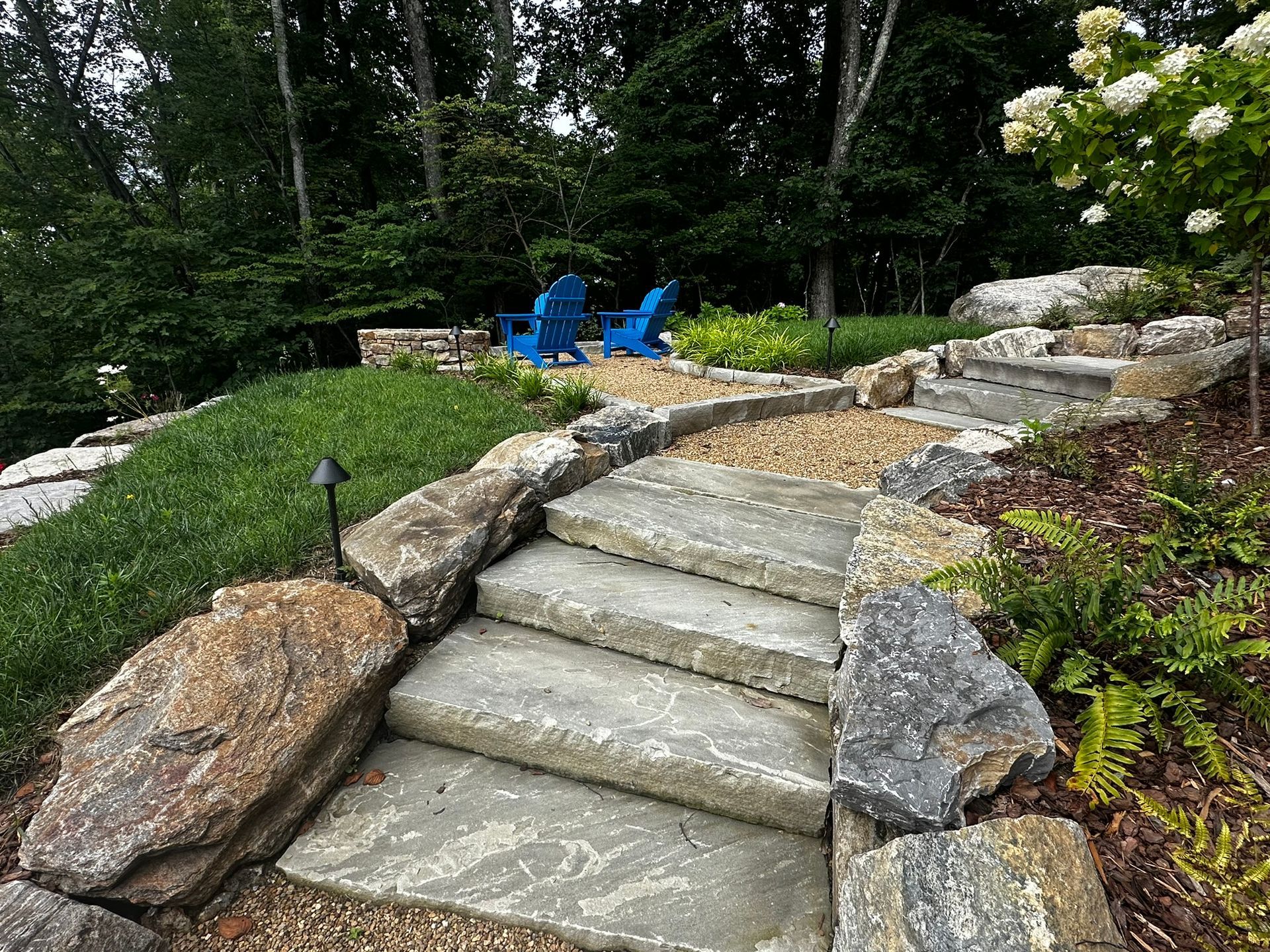A set of stairs leading up to a rocky area with blue chairs in the background.