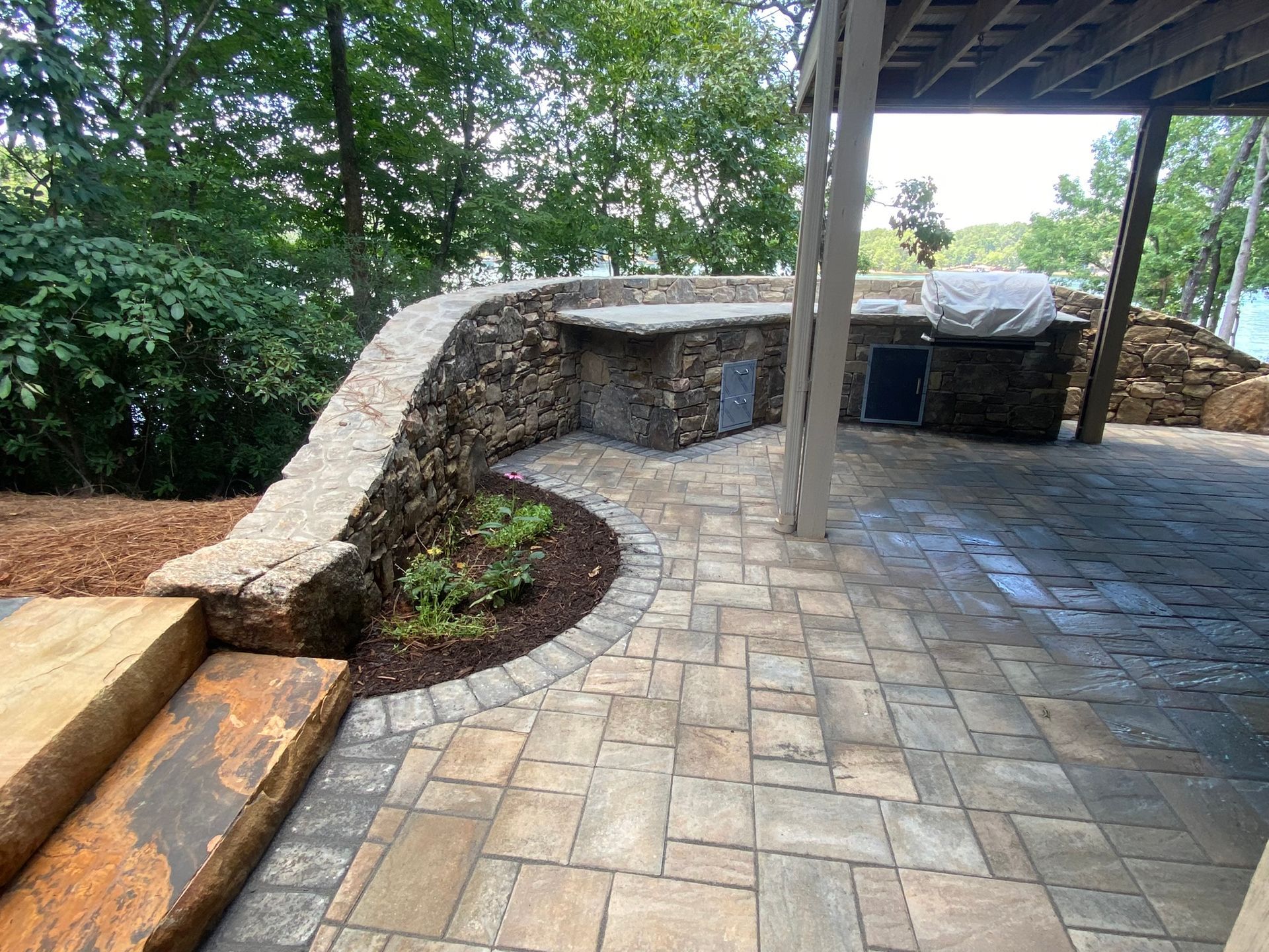 A patio with a stone wall, stairs, and a grill.