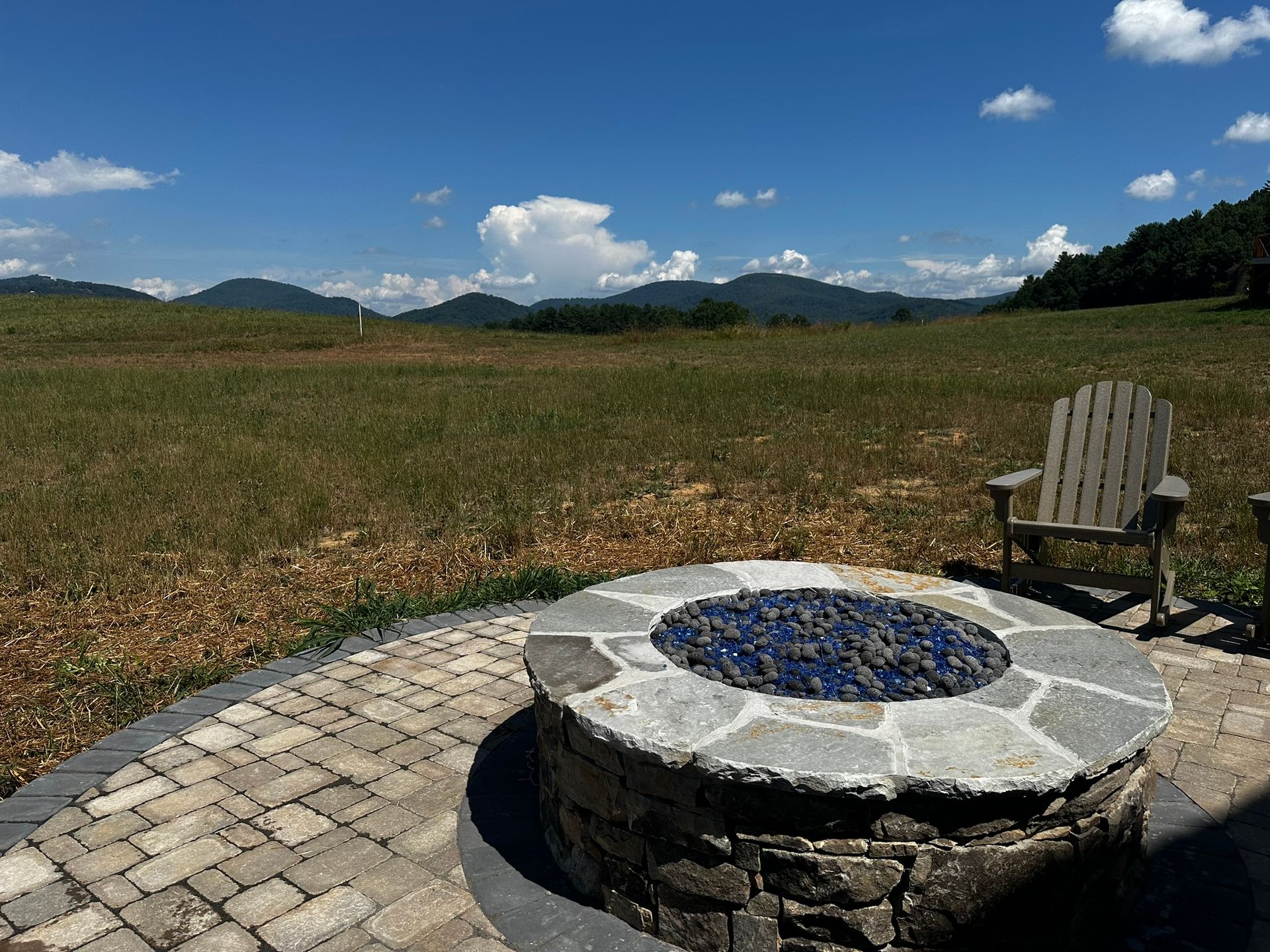 There is a fire pit in the middle of a field with mountains in the background.