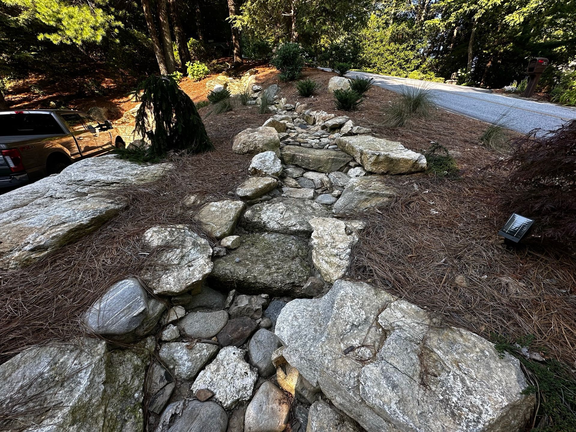A rocky path leading to a gravel road in the woods.