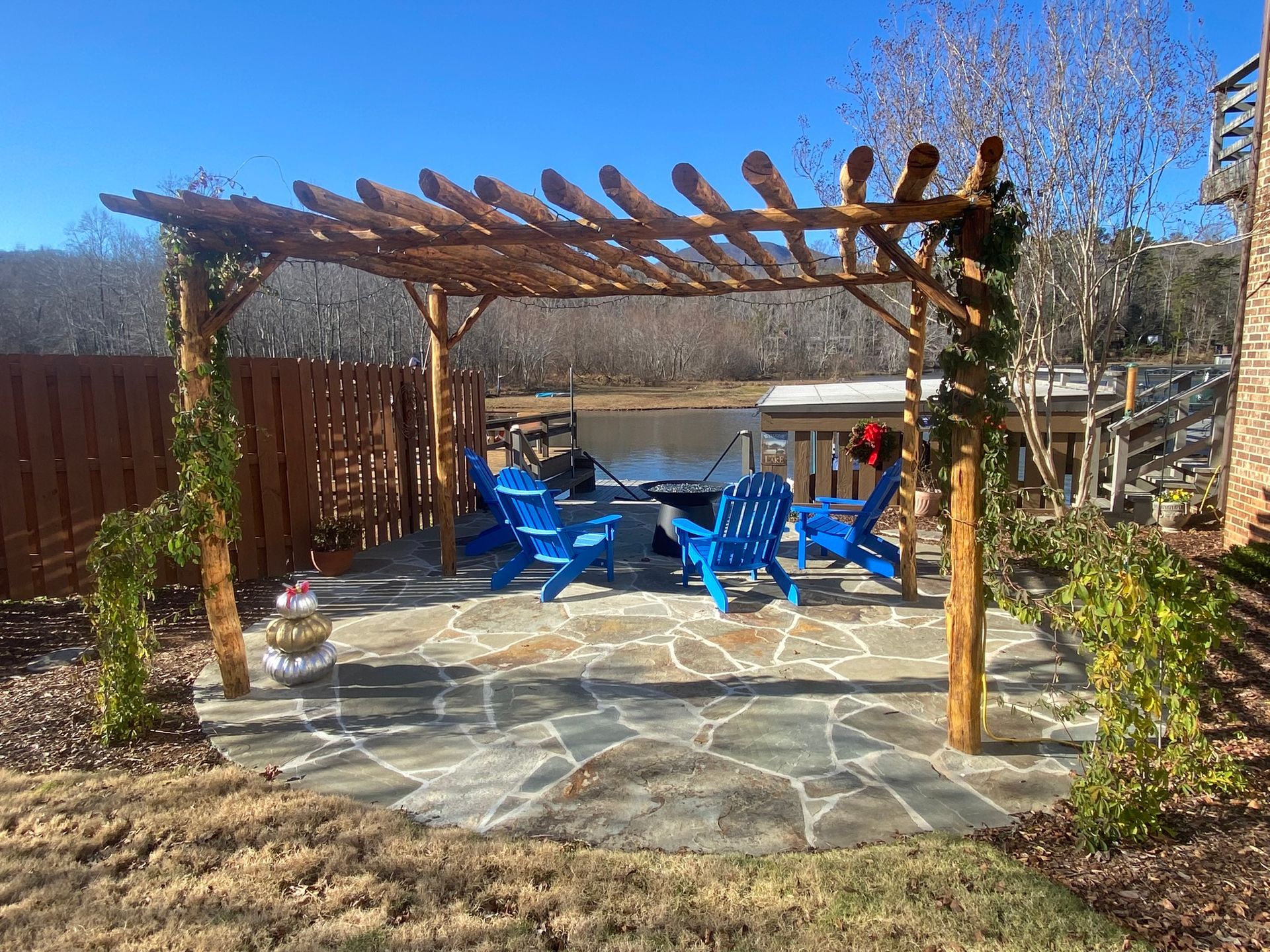 A pergola with blue chairs and a fire pit in the backyard.