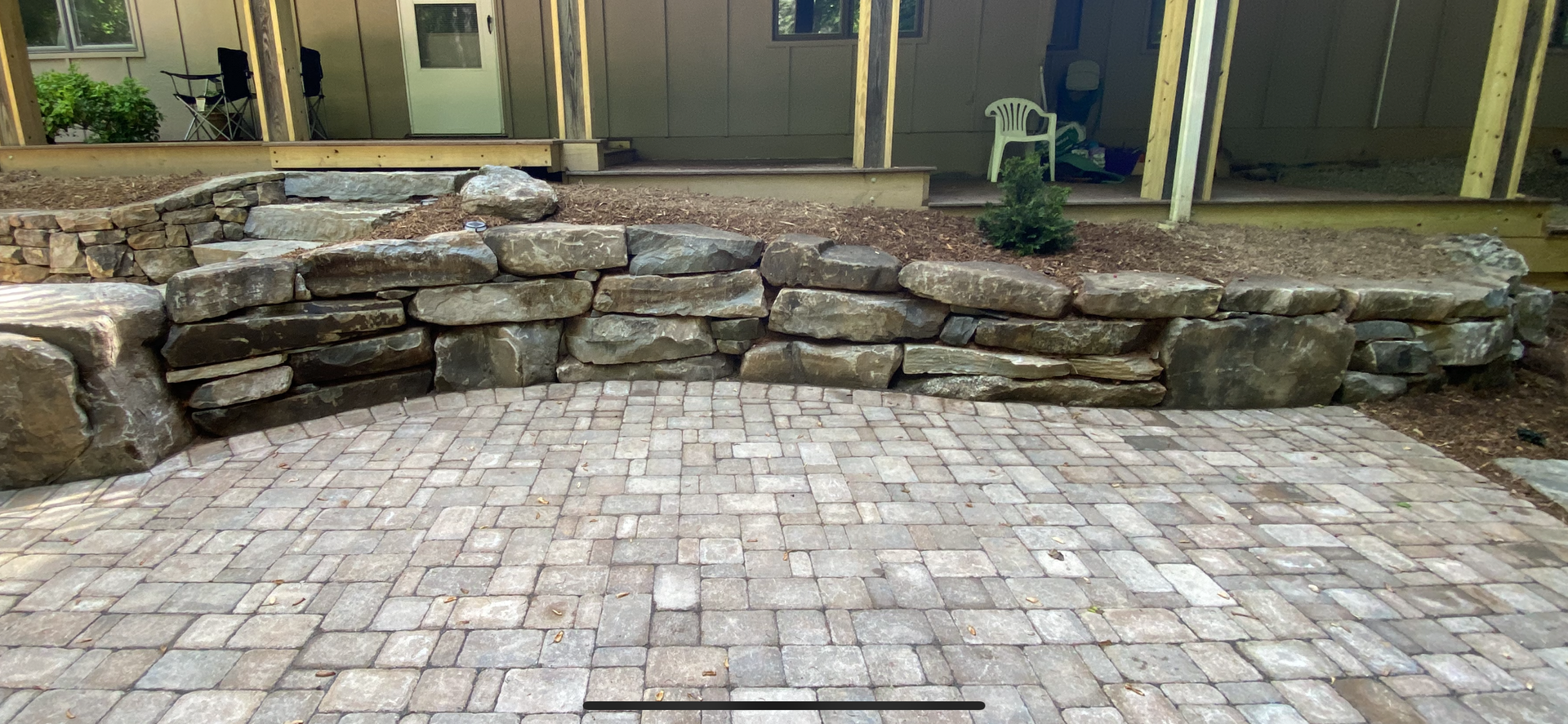 A stone wall surrounds a brick patio in front of a house.
