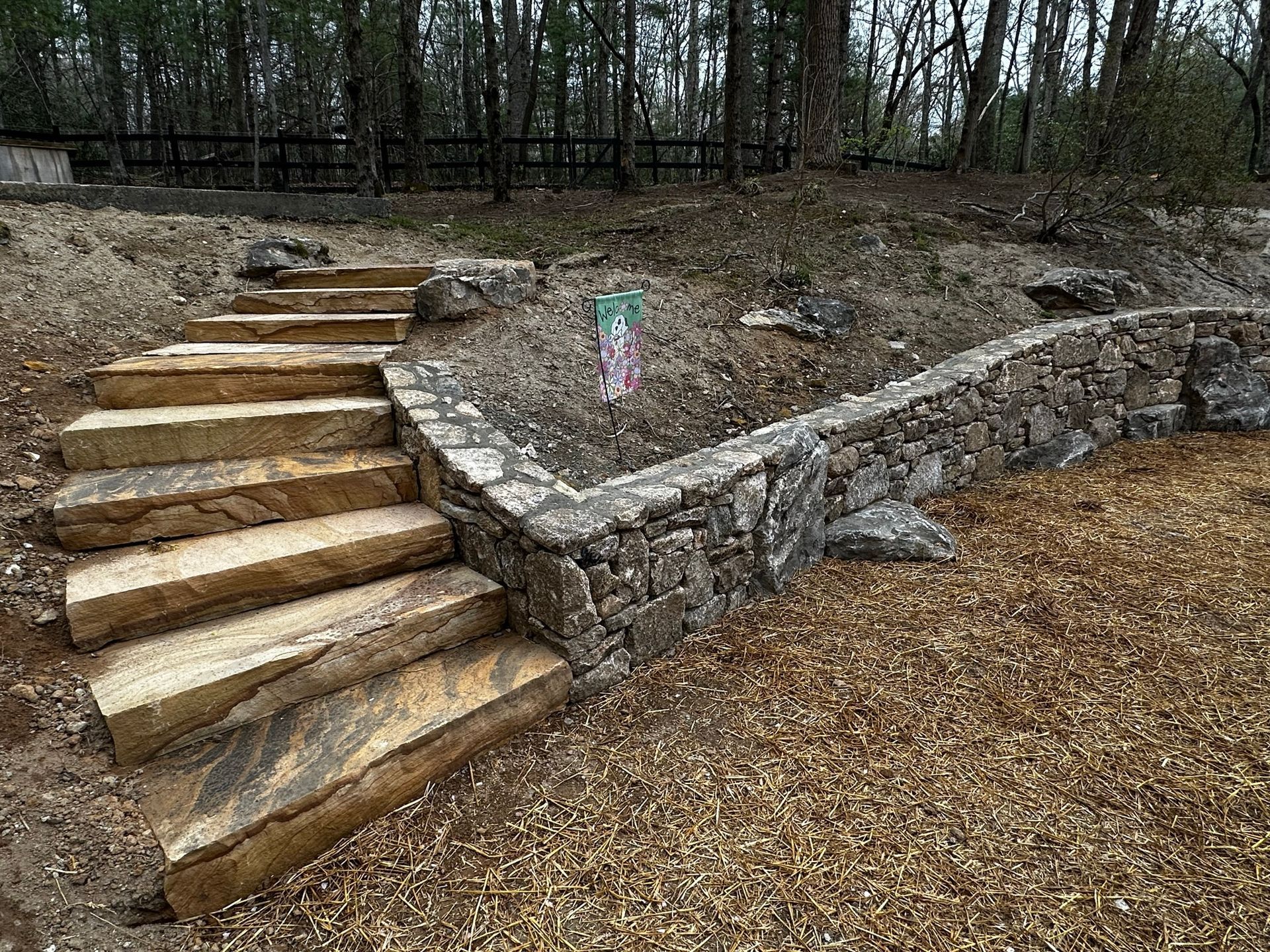 A set of stairs leading up to a stone wall in the woods.