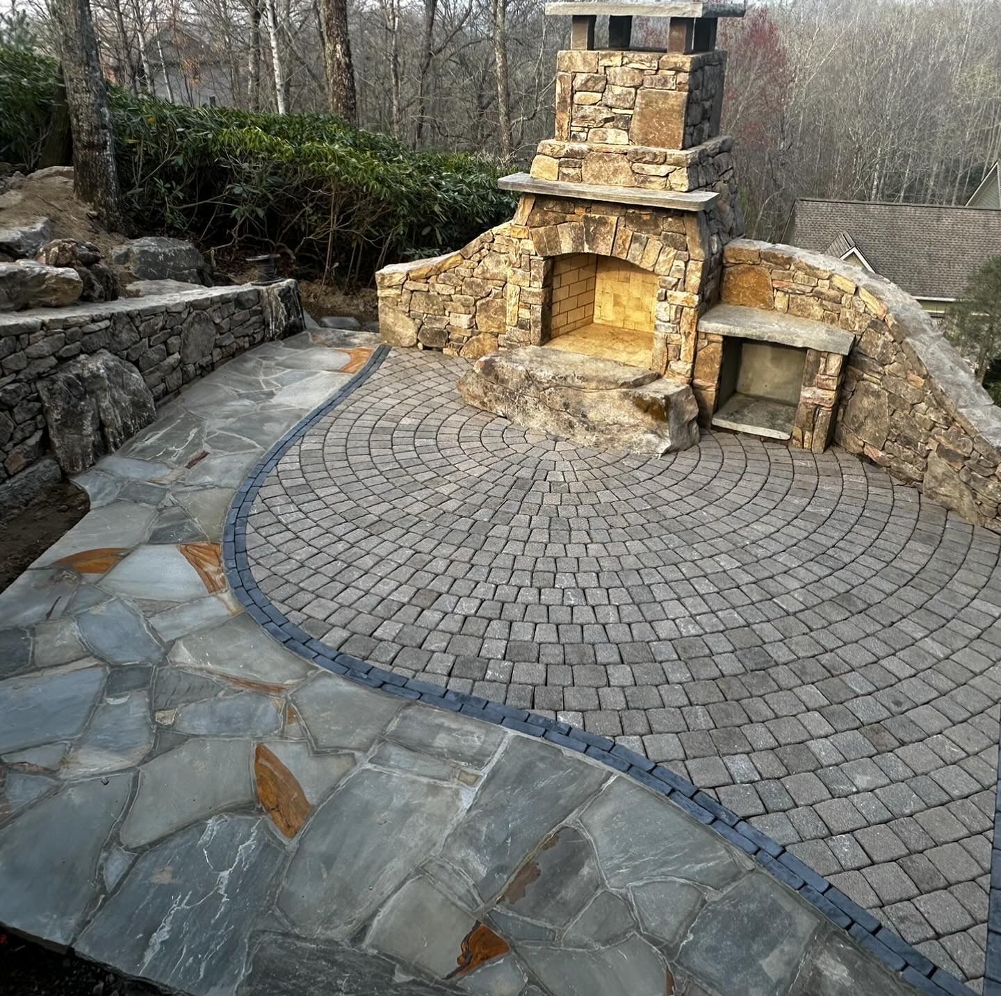 A stone fireplace sits in the middle of a brick patio.