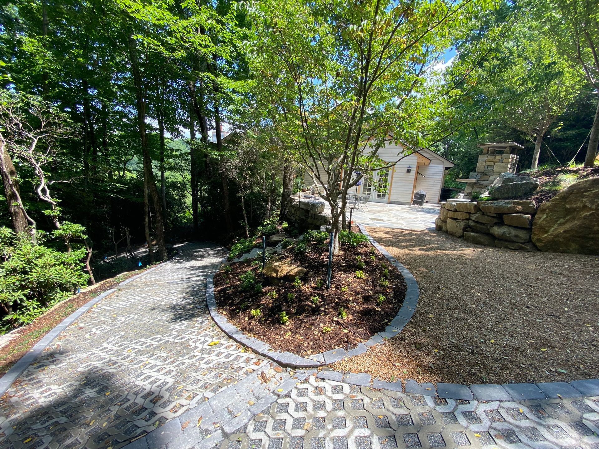 A driveway leading to a house surrounded by trees and rocks.