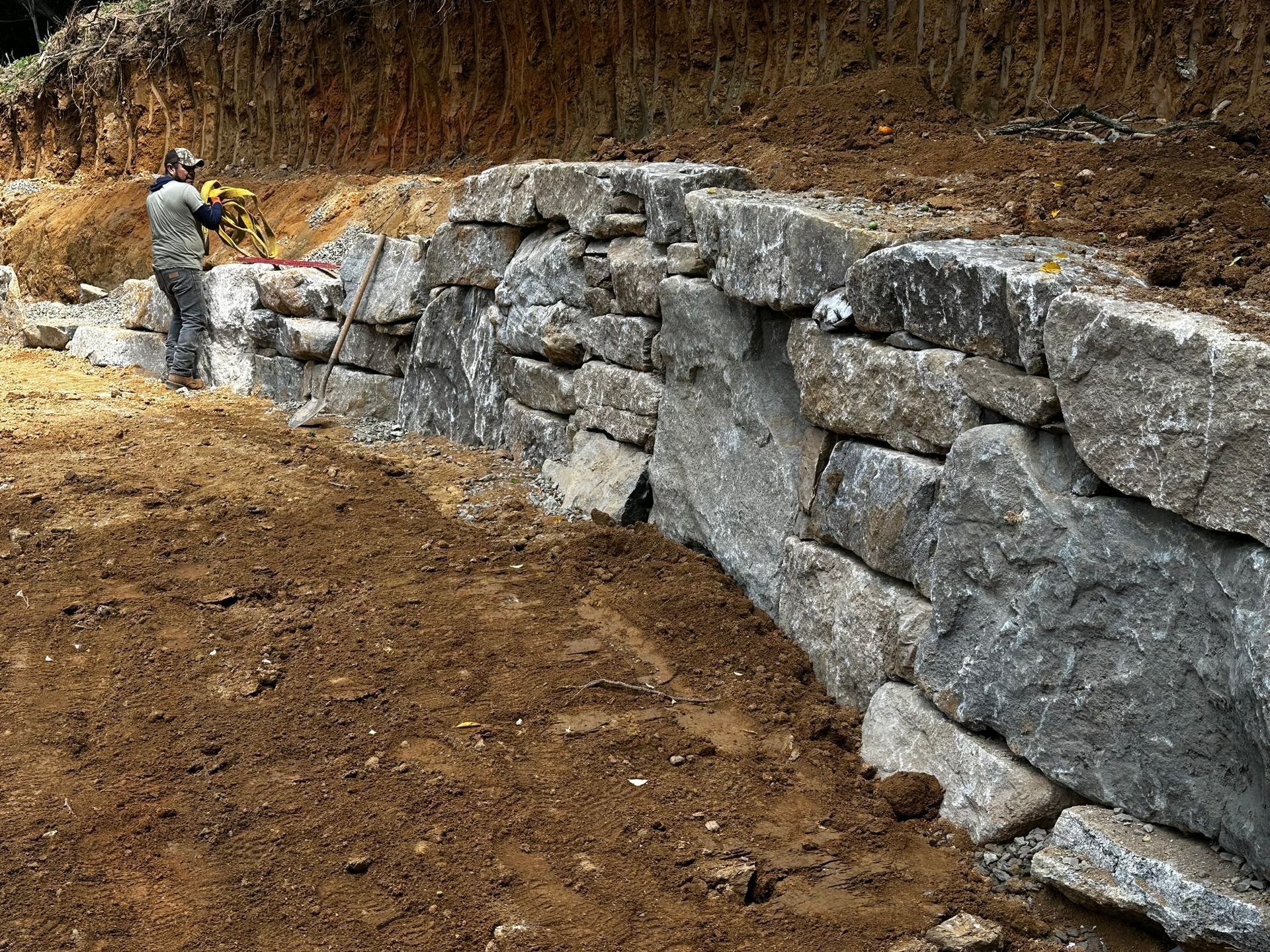 A man is standing next to a large rock wall.