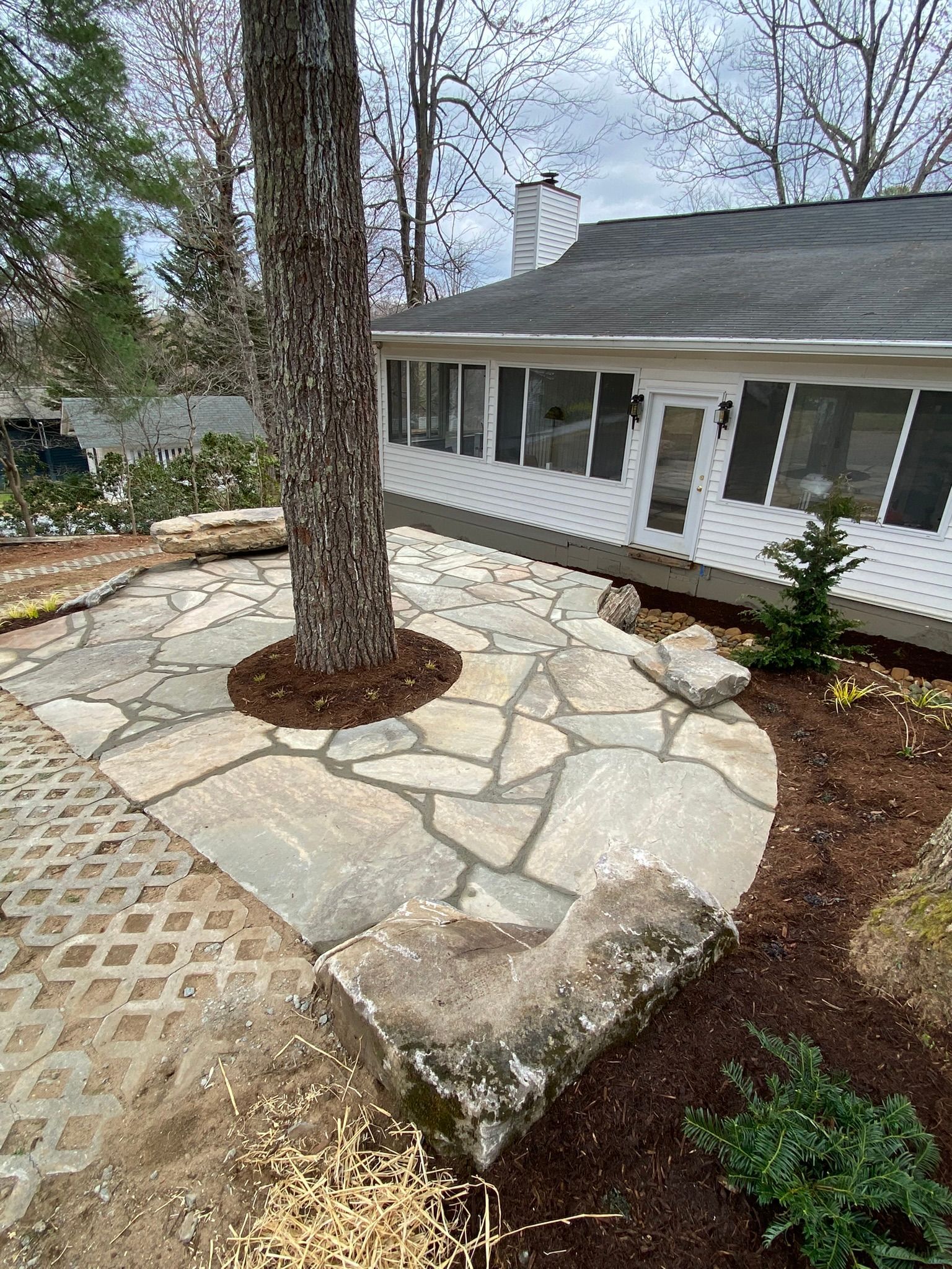 A stone patio with a tree in the middle of it in front of a house.