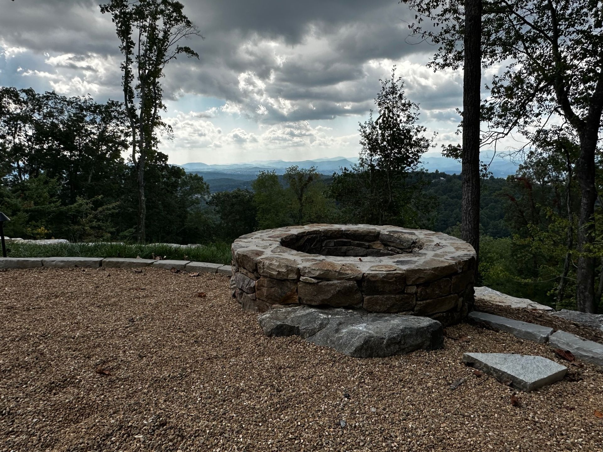 A fire pit in the middle of a gravel area with trees in the background.