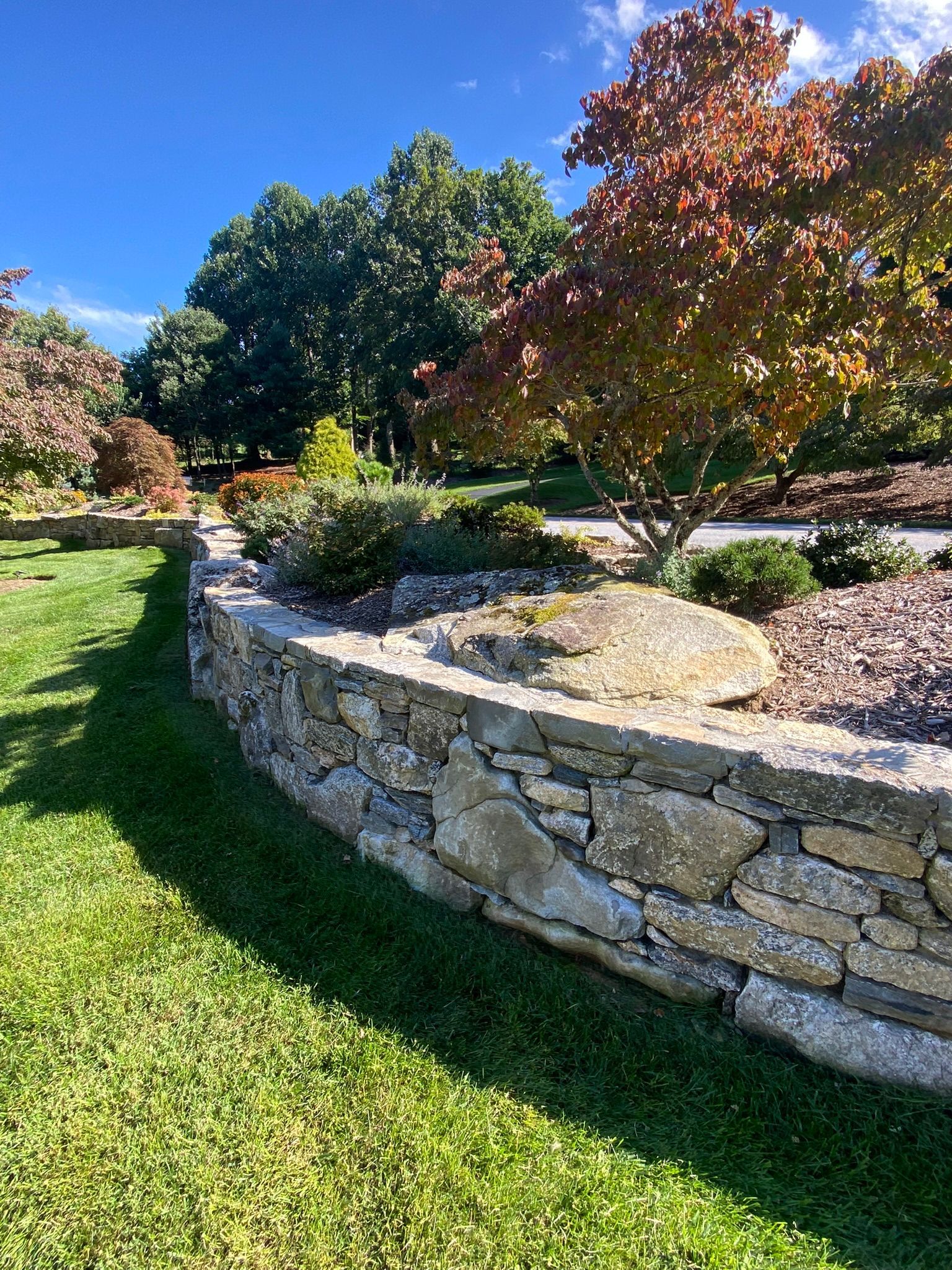 A stone wall surrounds a lush green lawn in a park.